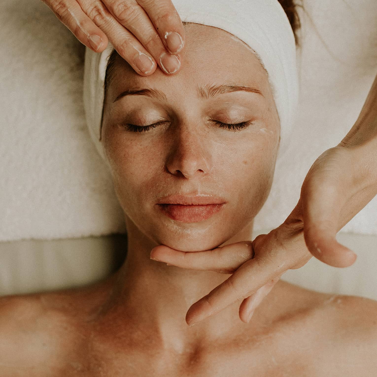 Person receiving a relaxing facial massage with eyes closed and head wrapped in a towel