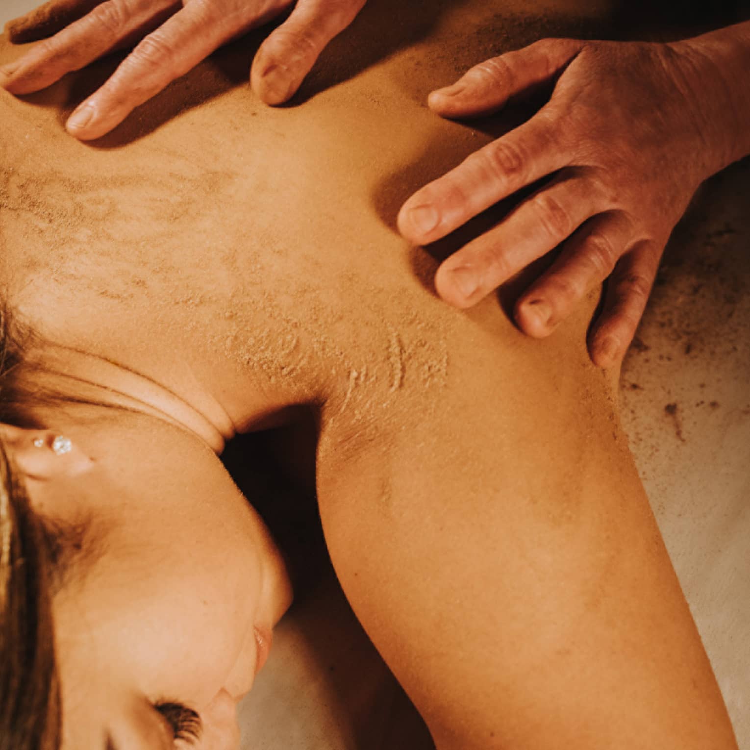 Two hands on woman's bare back as she lays on massage table in dimly lit room