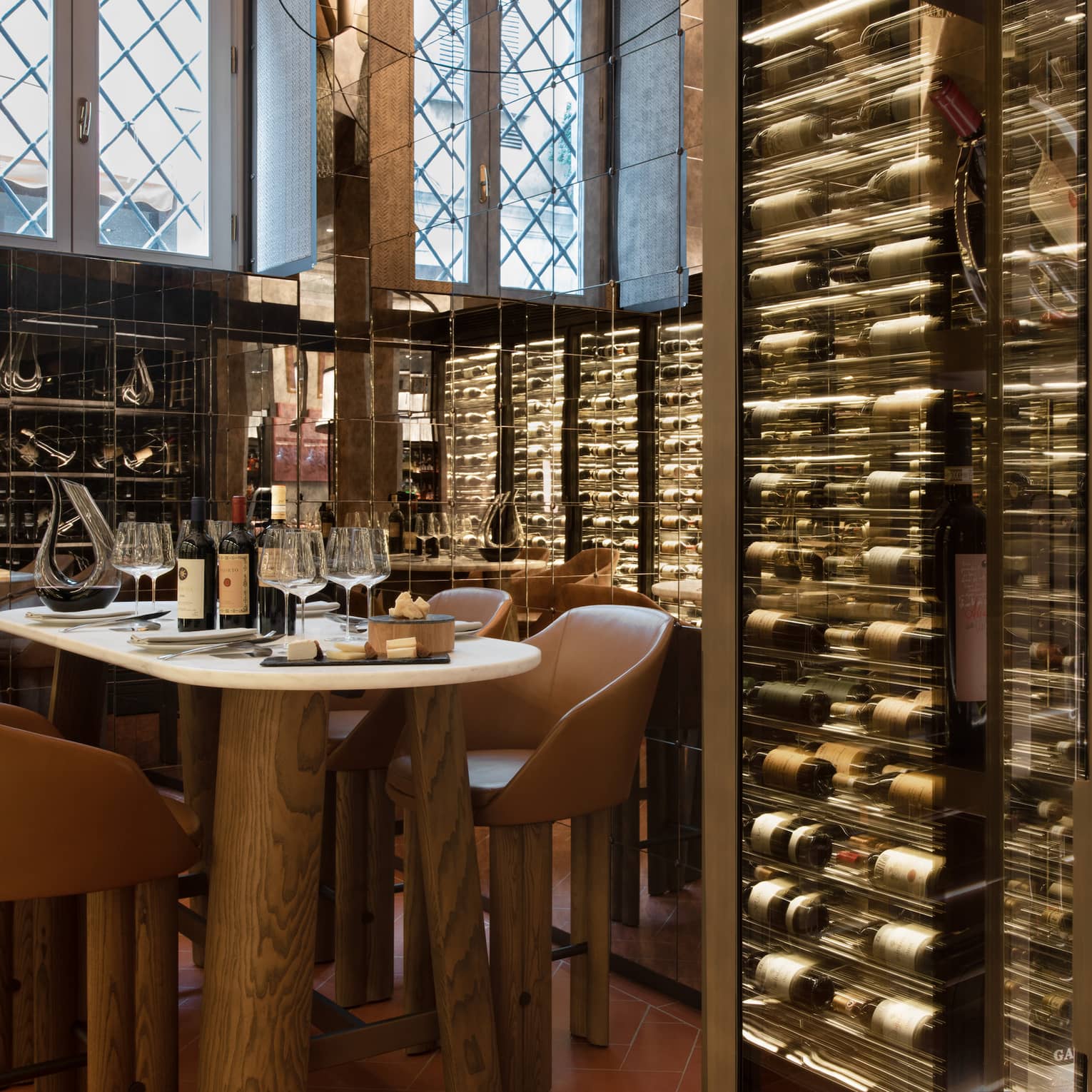 A table for four set within the mirrored walls of a wine cellar stocked with bottles displayed horizontally in glass cases.