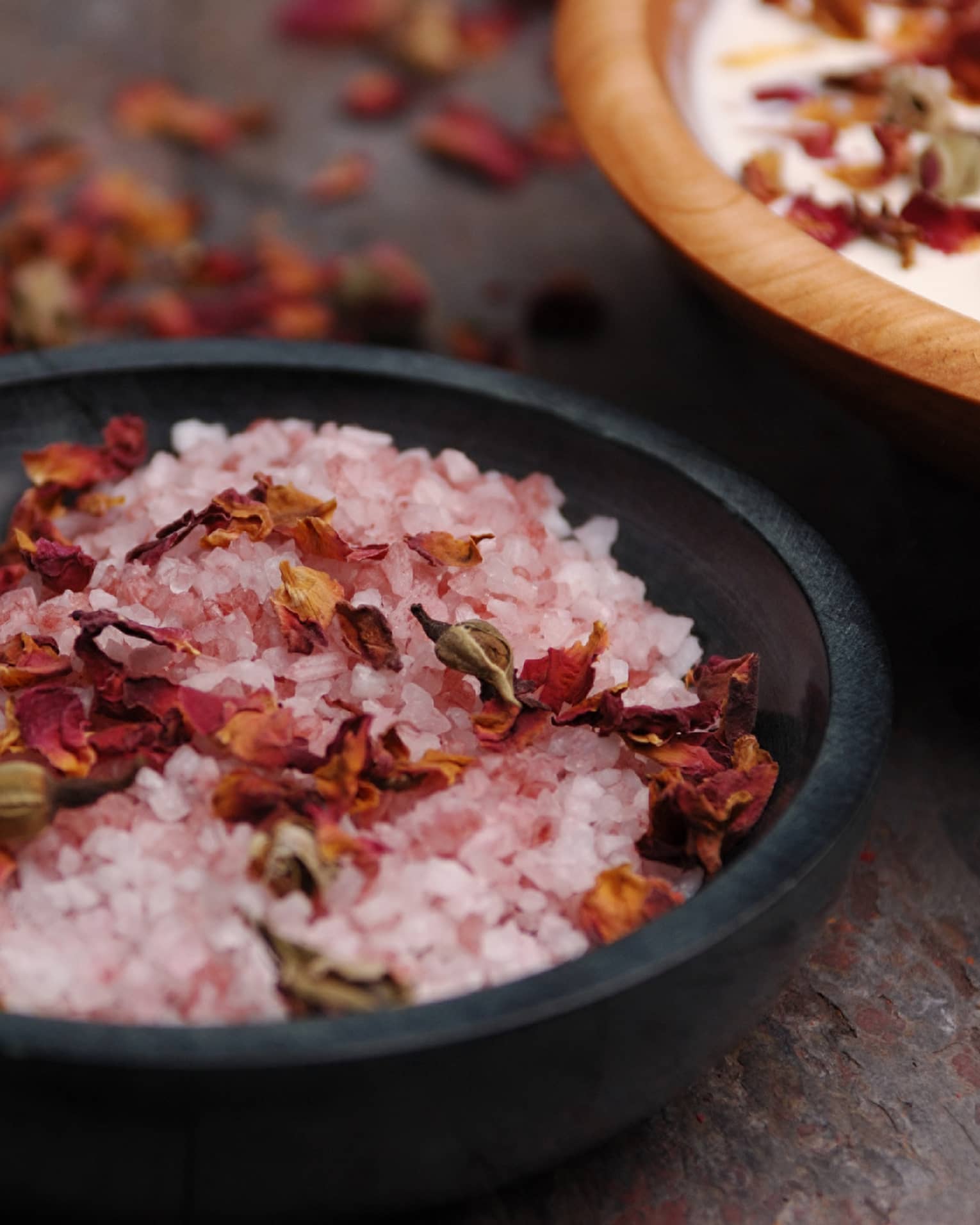 Pink crystals or salt and red flowers in a black bowl.