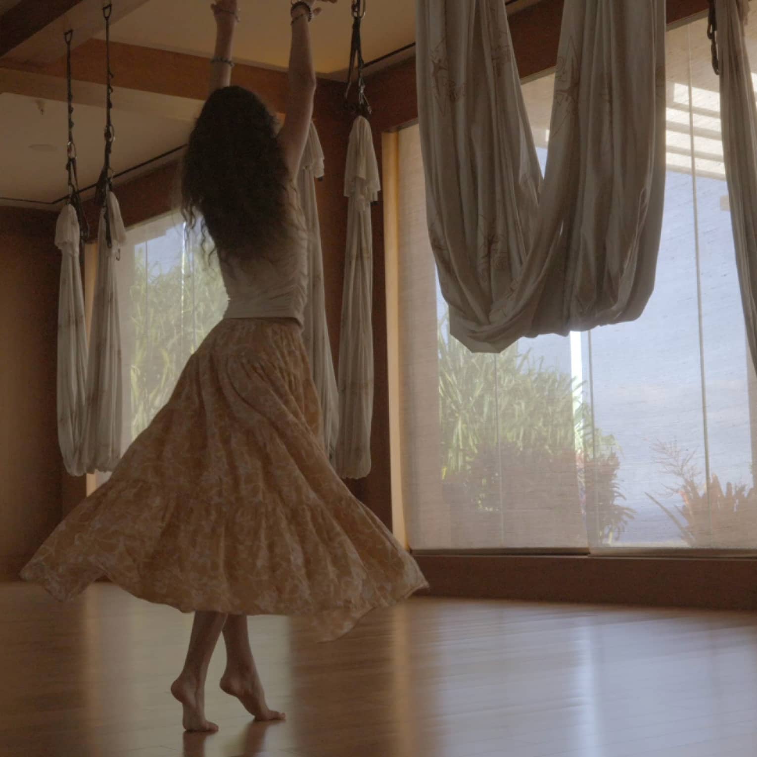 A woman dances in movement studio featuring hanging aerial yoga hammocks