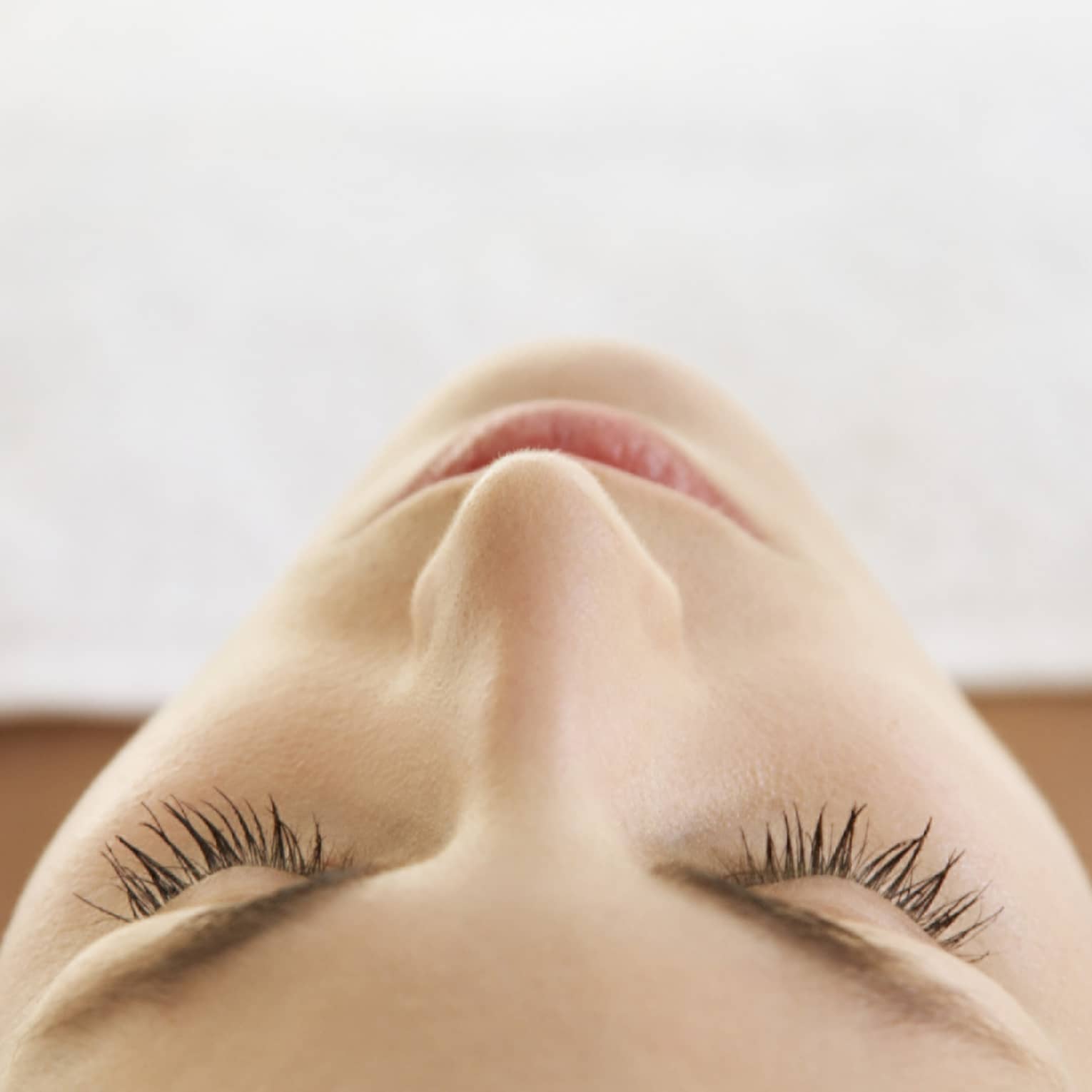 Woman lying down with eyes closed, bare shoulders, covered with white sheet