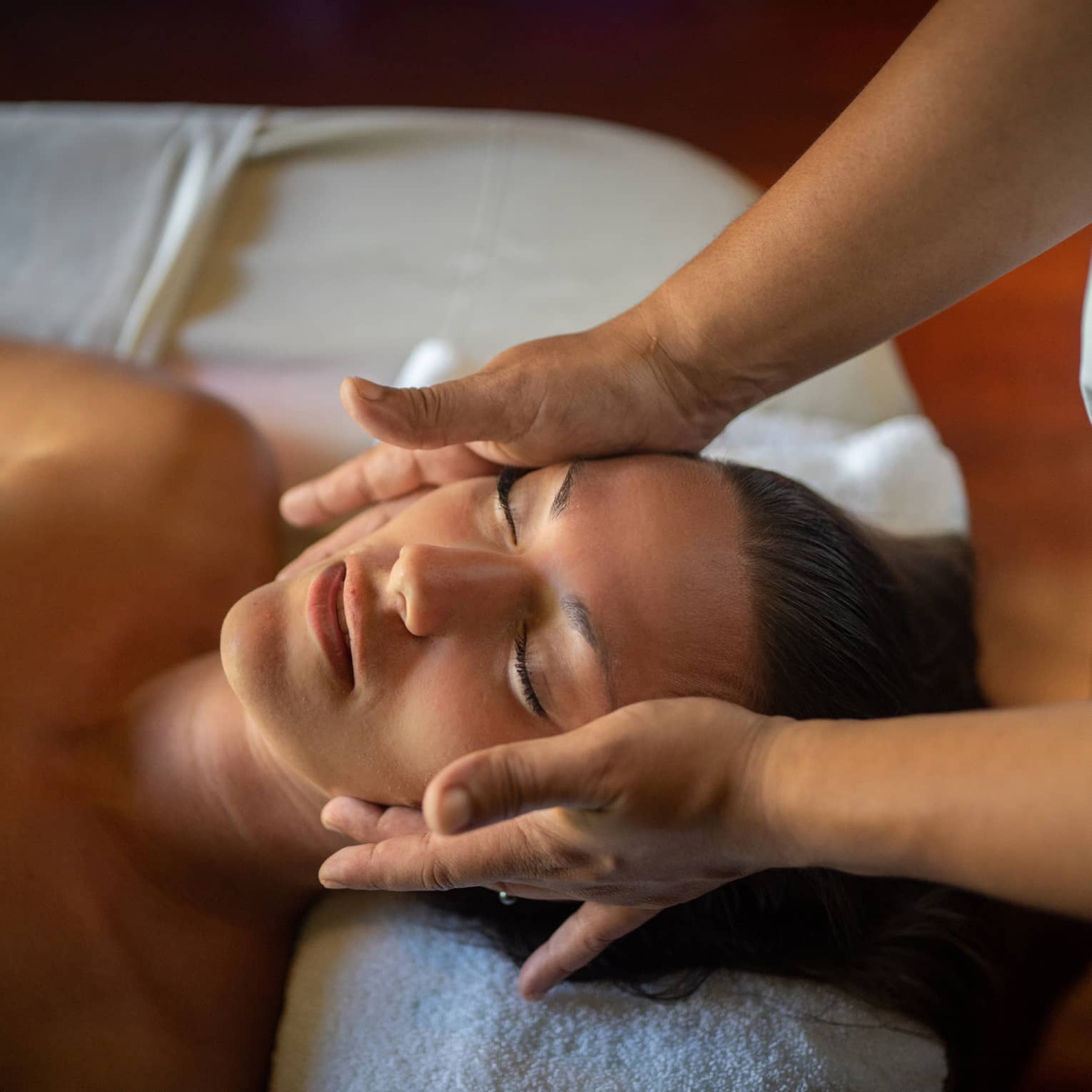 Woman lays on massage table with eyes closed as hands massage her cheeks and chin