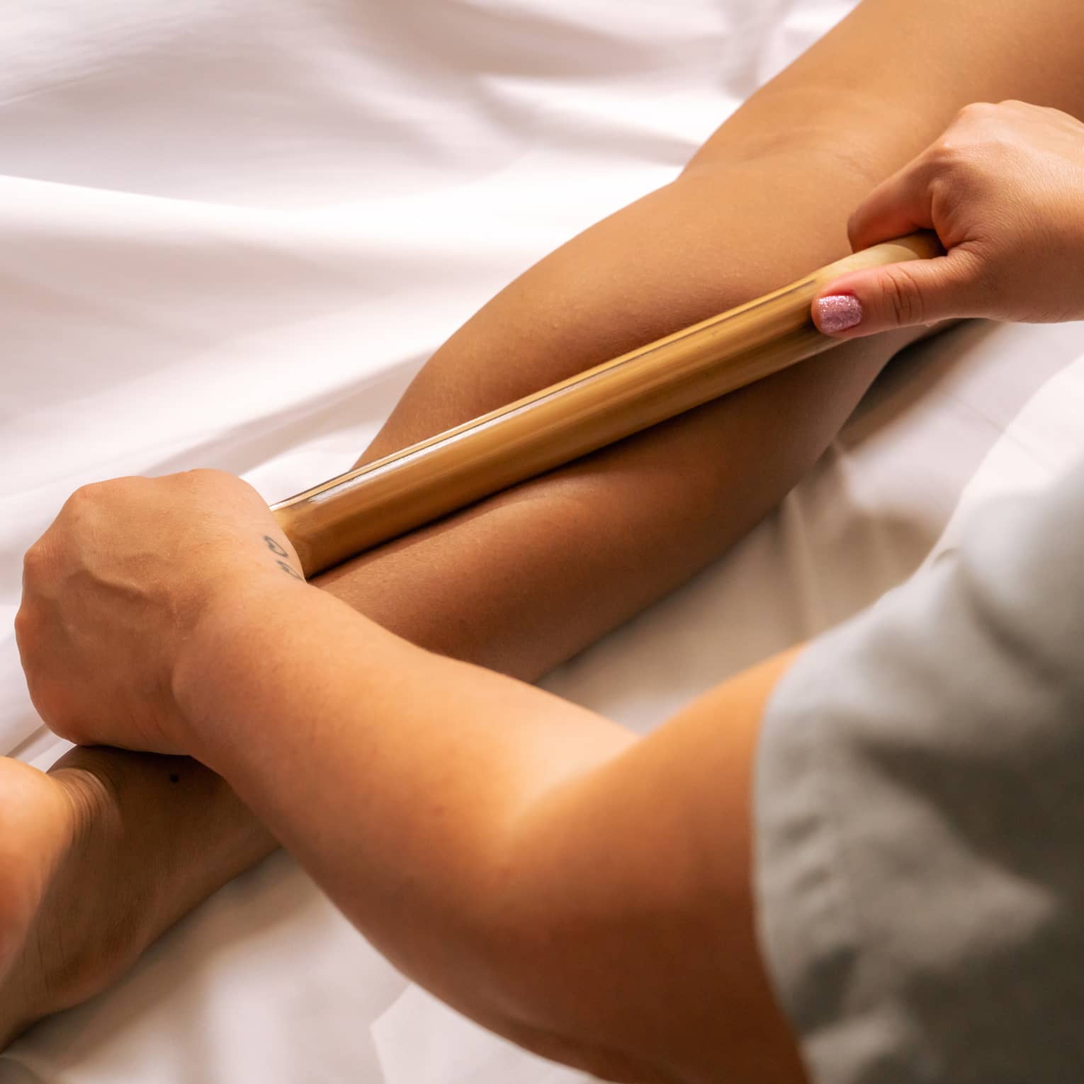 Pair of hands rolling a bamboo stick over a person's calf muscle