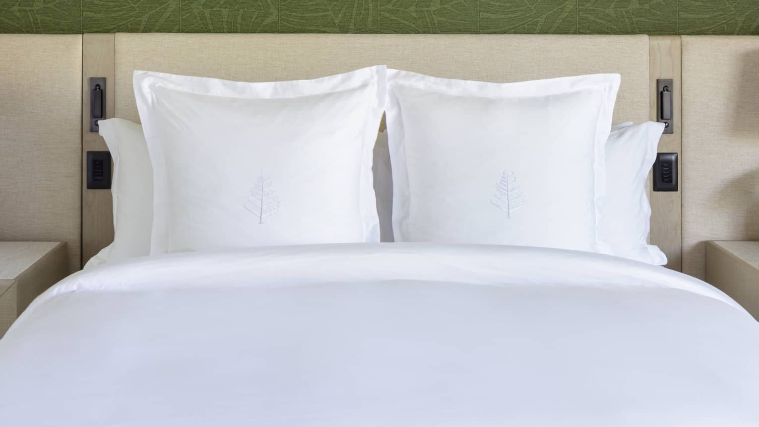 King bed with white sheets and Four Seasons logo on the pillows, set against green wallpaper