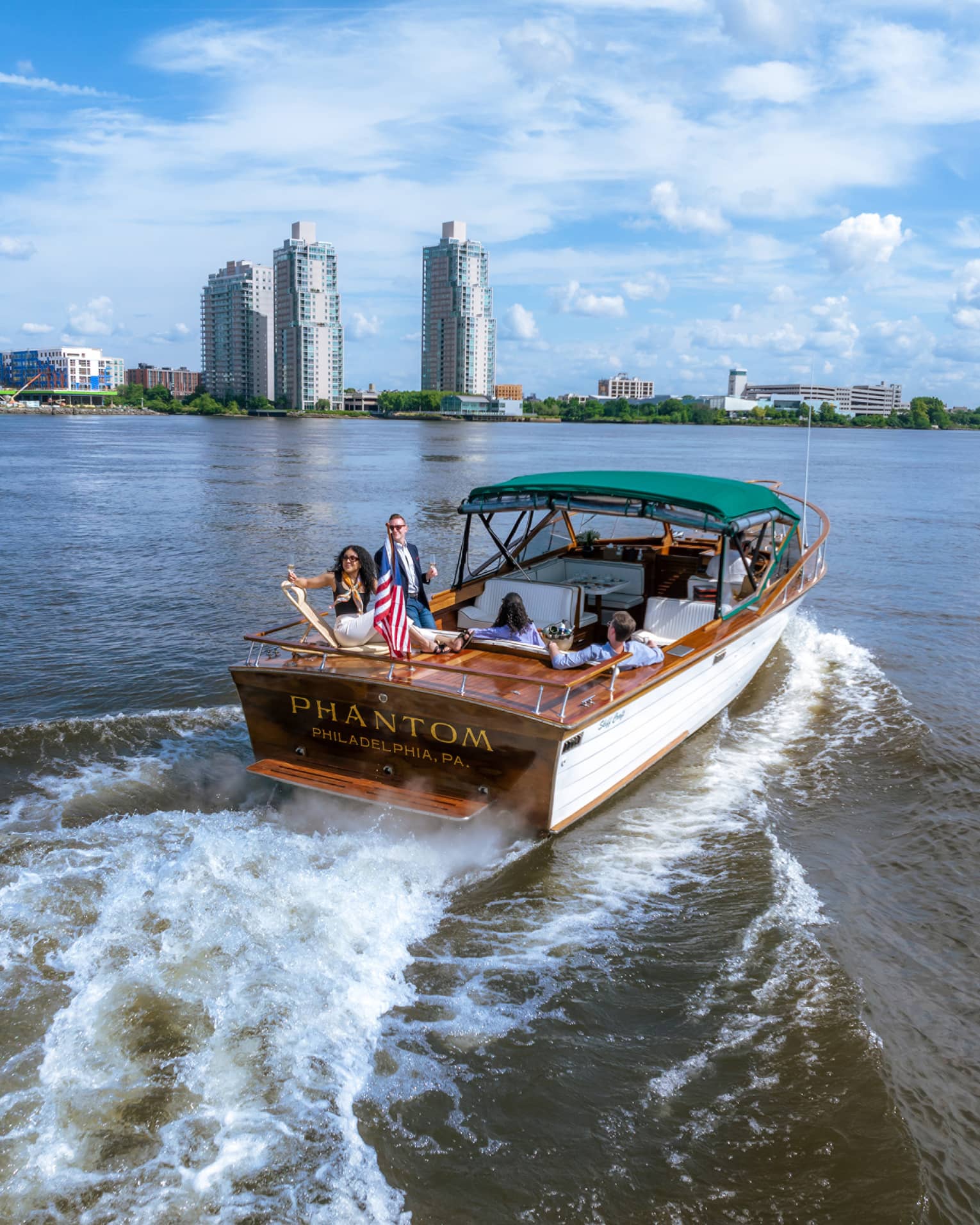 Guests on a boat in the water with city buildings in the background.
