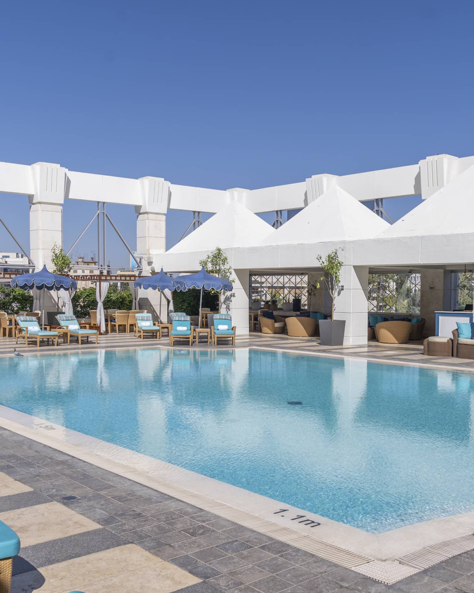 Outdoor pool surrounded by blue lounge chairs and four white tents