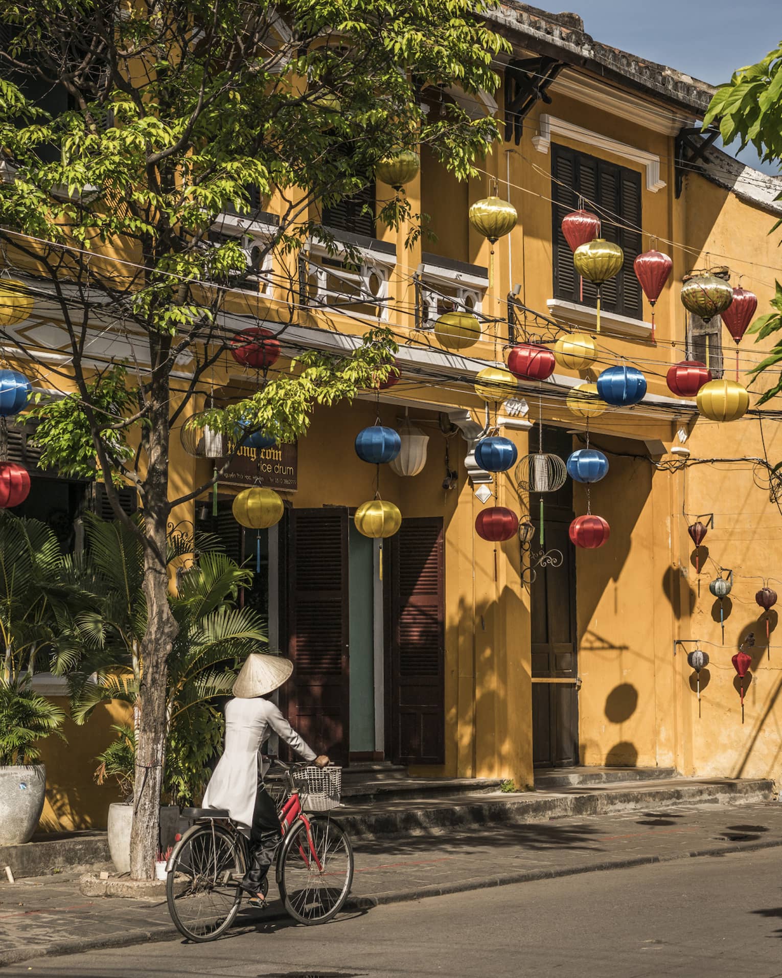A woman biking down a historic street in Hoi, Viet Nam with lanterns along the side of a house