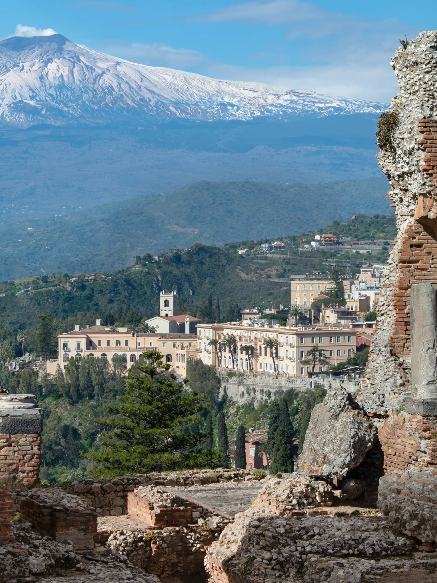 View of ancient stone ruins with a distant town and snow-capped mountains in the background.