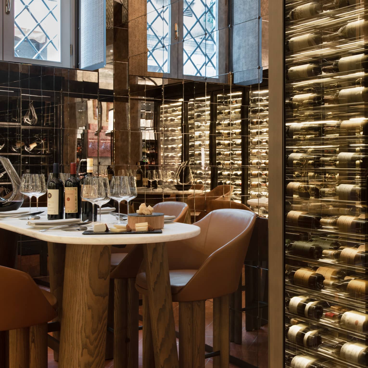 A table for four set within the mirrored walls of a wine cellar stocked with bottles displayed horizontally in glass cases.