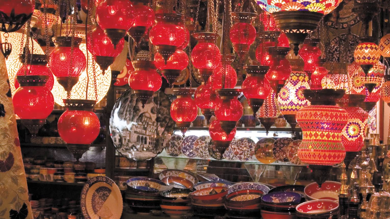 Red lanterns hang over shelves with decorative plates in Grand Bazaar