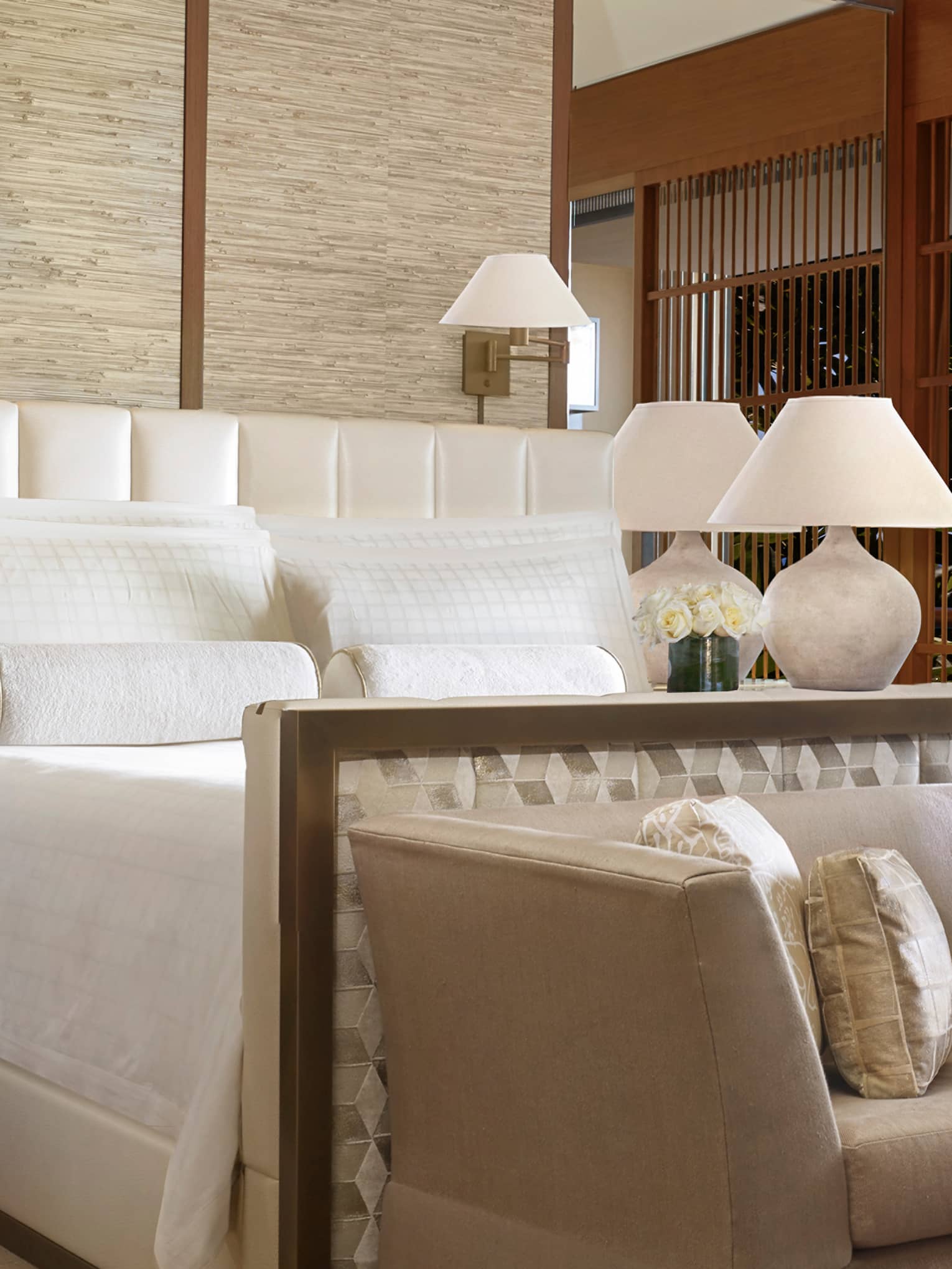 Makai Suite hotel bed, dresser with white flowers, lamp, small plush sofa and silk pillows at foot
