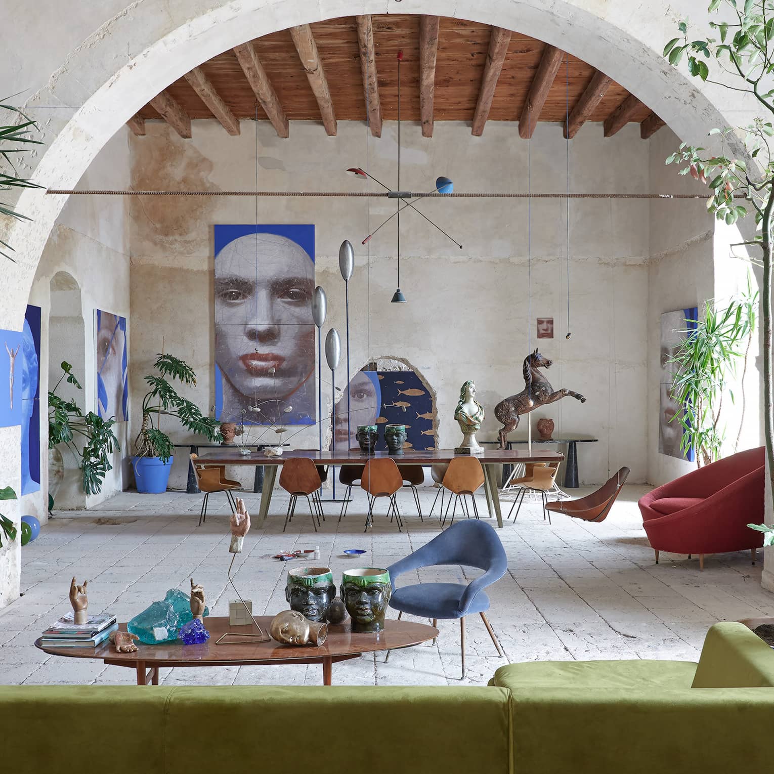 Large room with tropical plants, contemporary furnishings, an arched stone wall and artwork in the distance