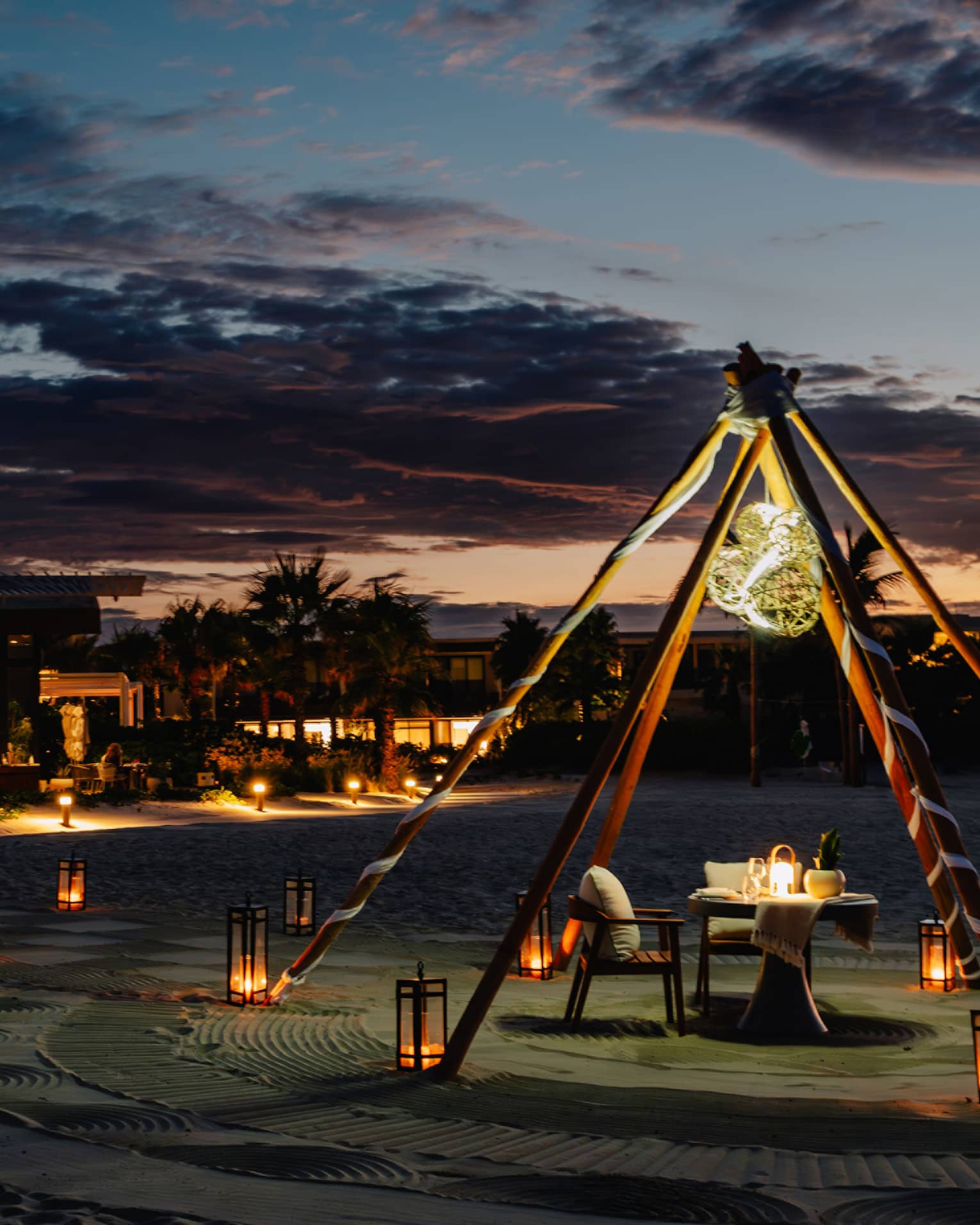 Outdoor tent with a chair and dining table, surrounded by lanterns on the ground in the evening.