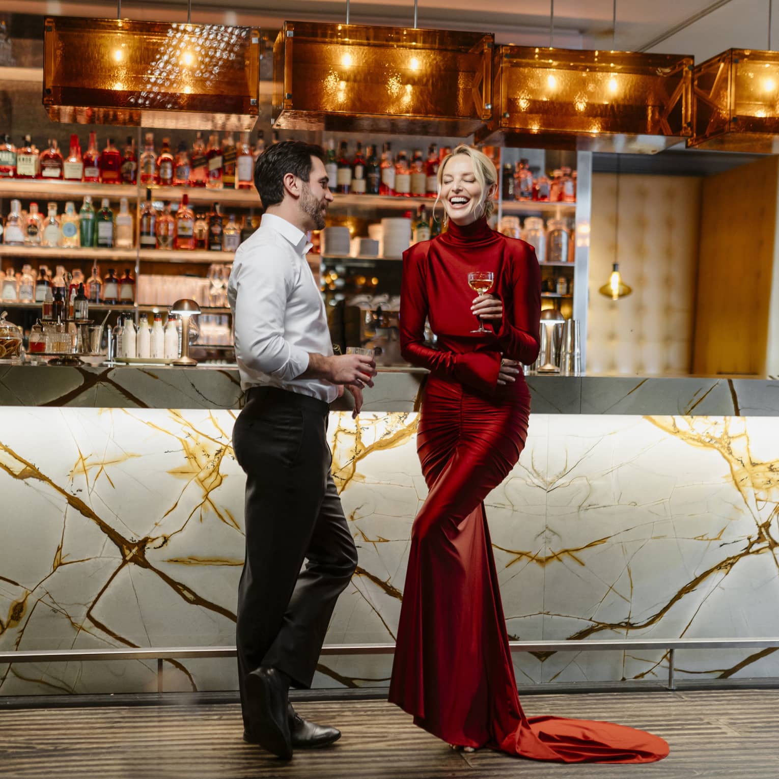 Couple standing, laughing in front of a dimly lit stocked bar