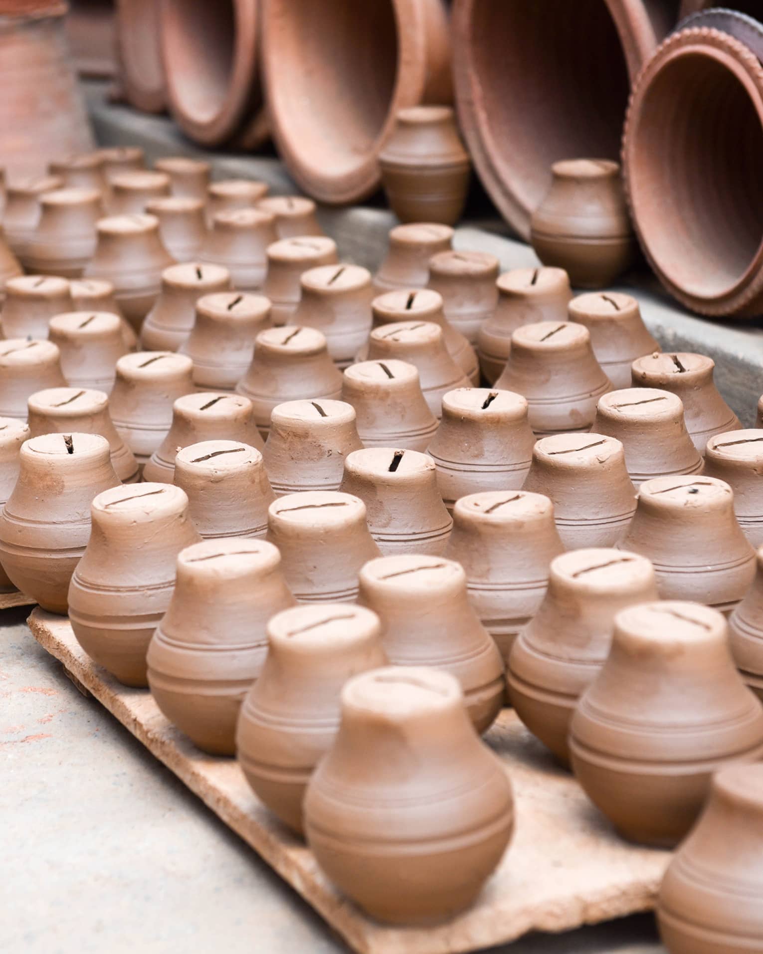 Close-up of dozens of small slit-topped clay pots arranged on wooden pallets alongside the open mouths of larger clay pots.