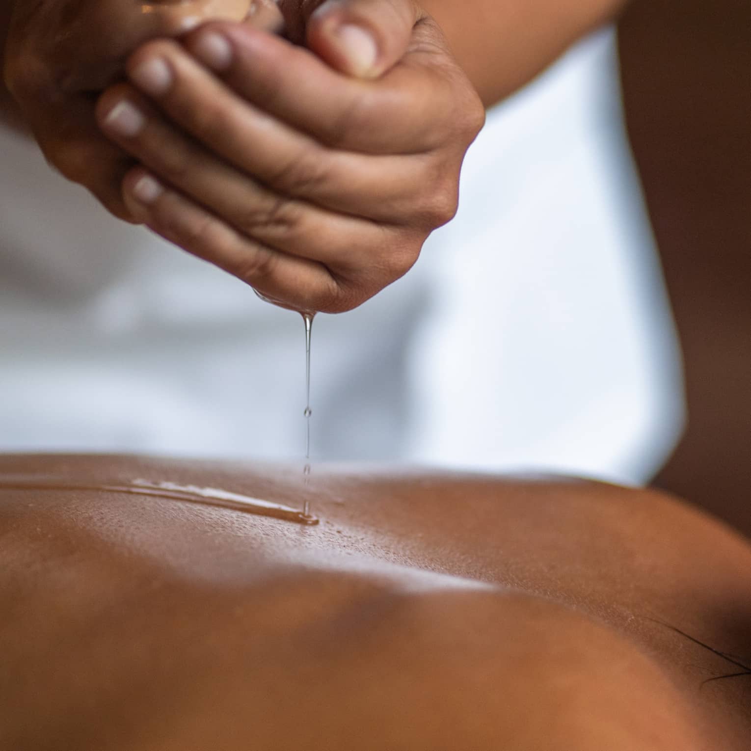 Delicate hands apply oil to a guest's back during a spa treatment