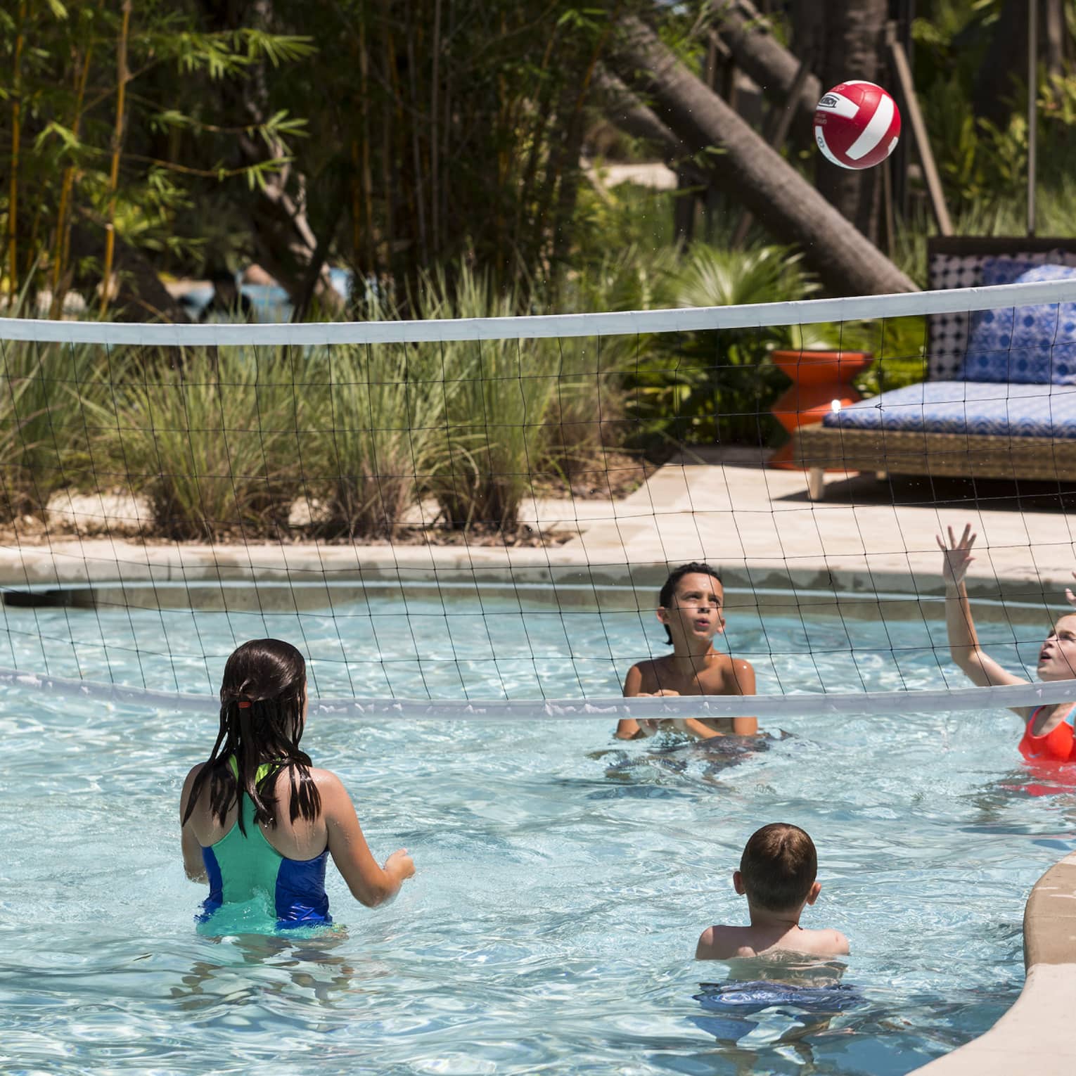 Kids play volleyball in small outdoor swimming pool with net