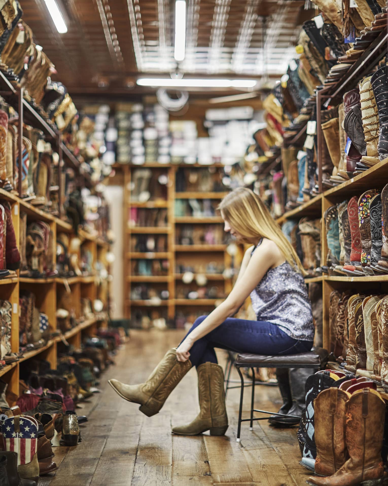 A woman trying on cowboy boots in a store full of them.