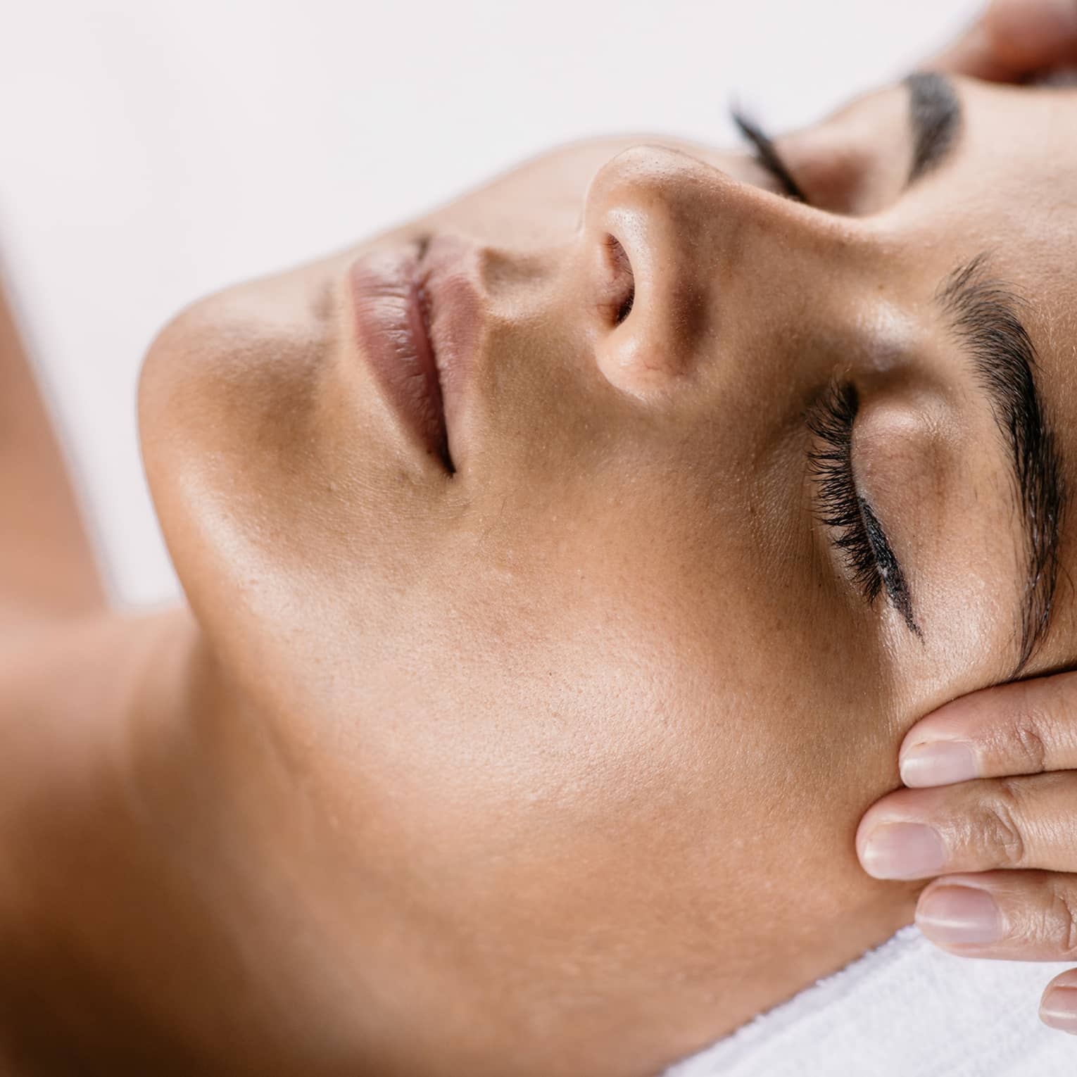 Hands massage woman's temples as she closes her eyes, spa towel around hair