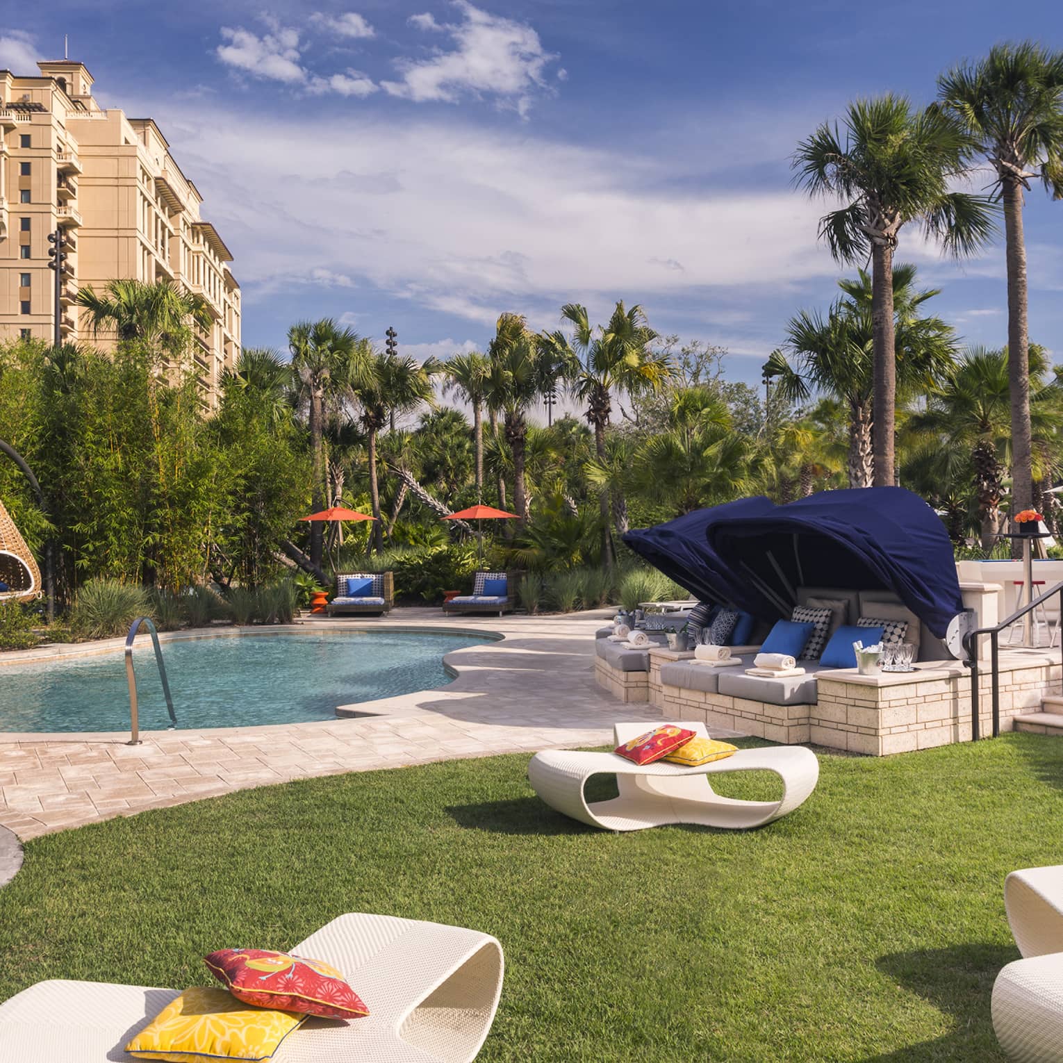 White patio chairs, hanging baskets, palm trees around swimming pool deck