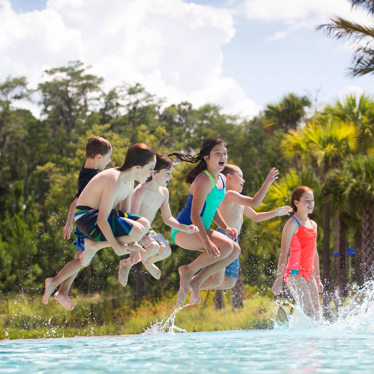 Group of children wearing swimsuits jump into outdoor swimming pool