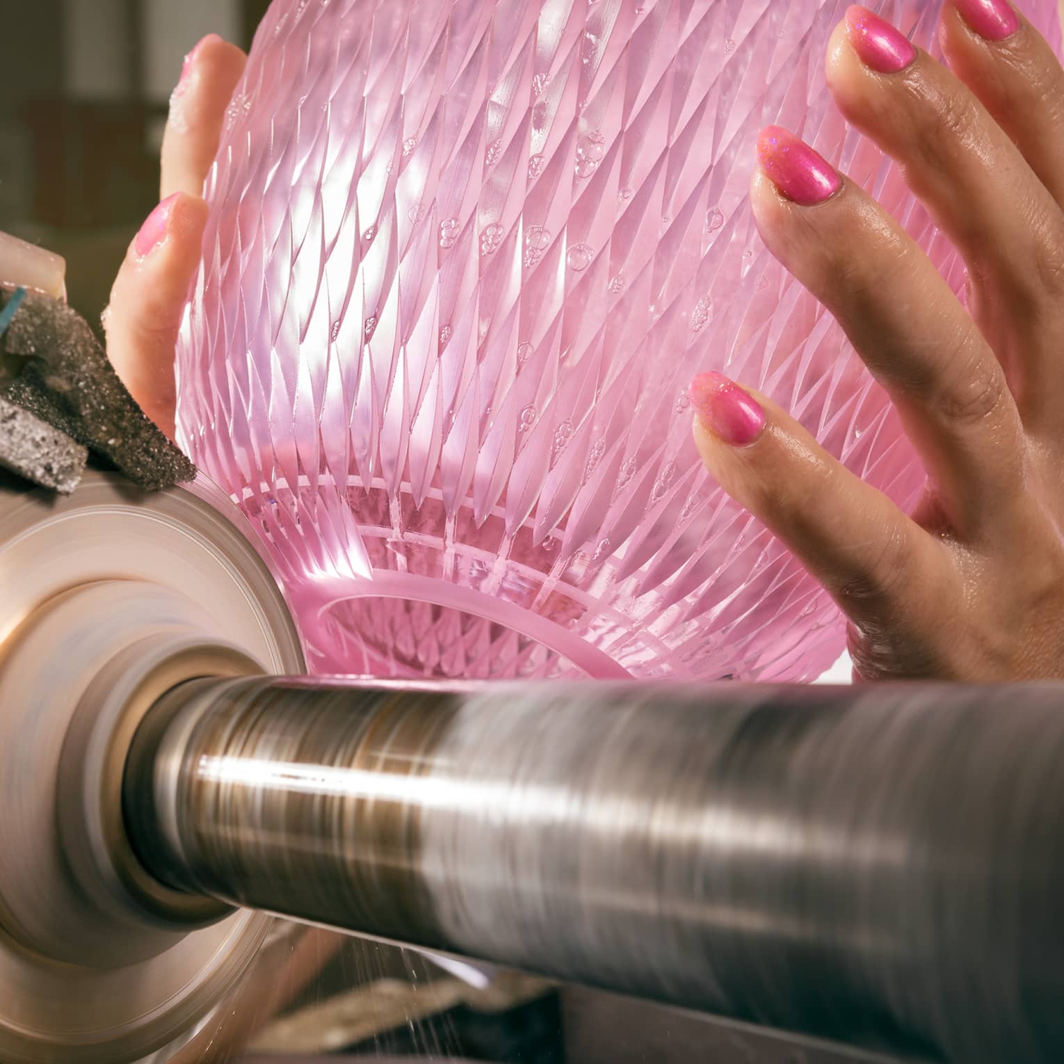 Hands with pink nails hold pink crystal vase atop glass-cutting machine