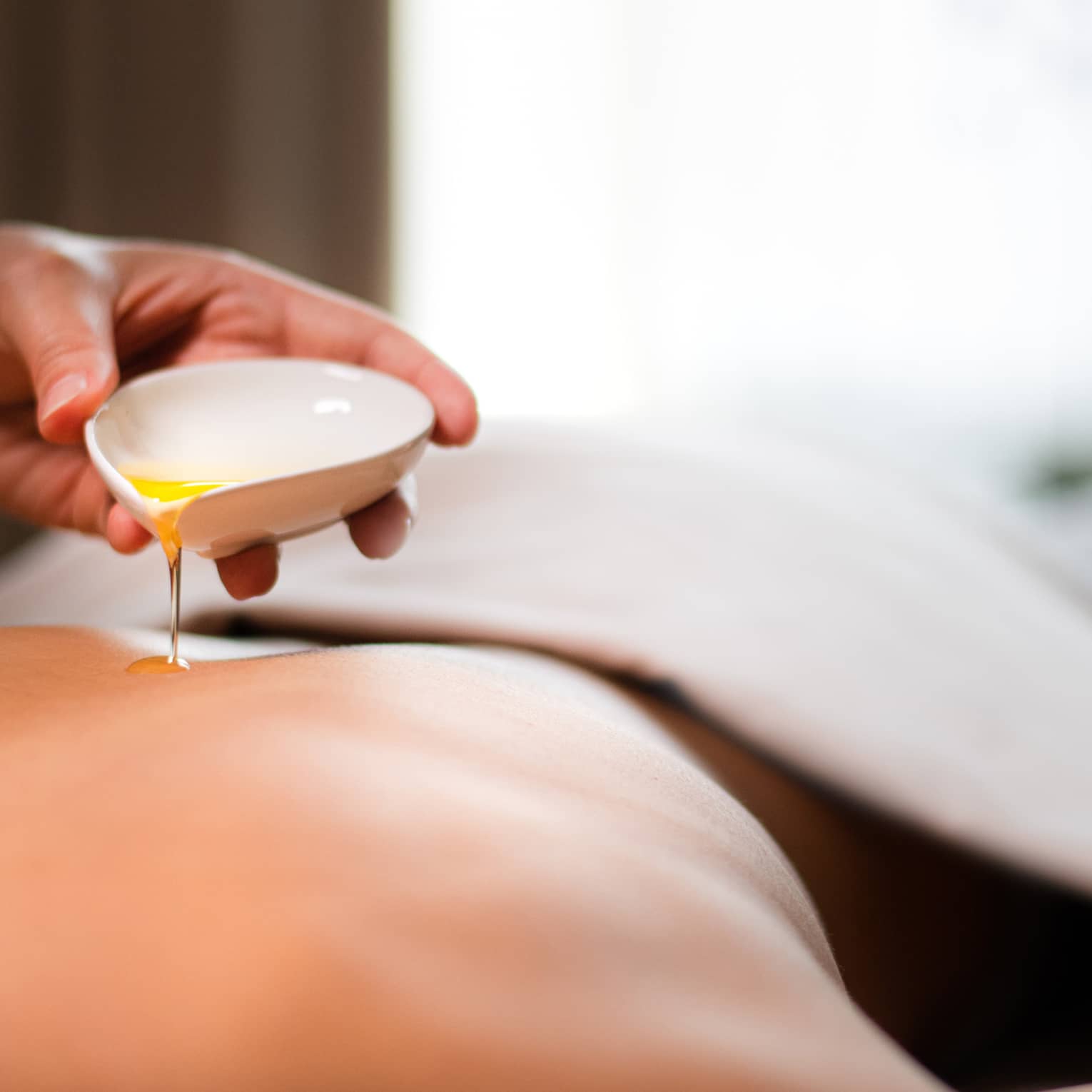 A spa staff member pouring liquid onto a woman?s back.