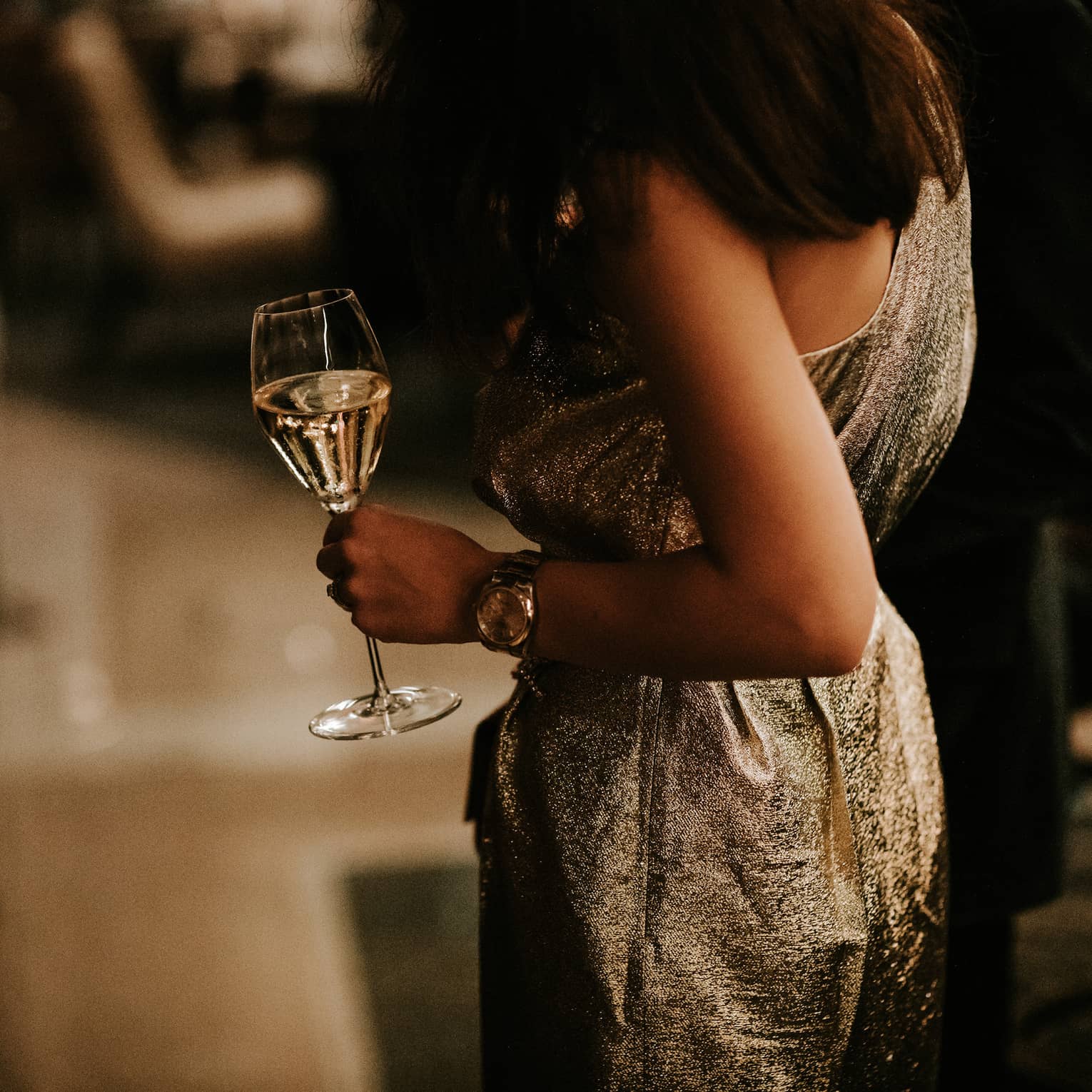 Woman in gold dress holding a glass of white wine