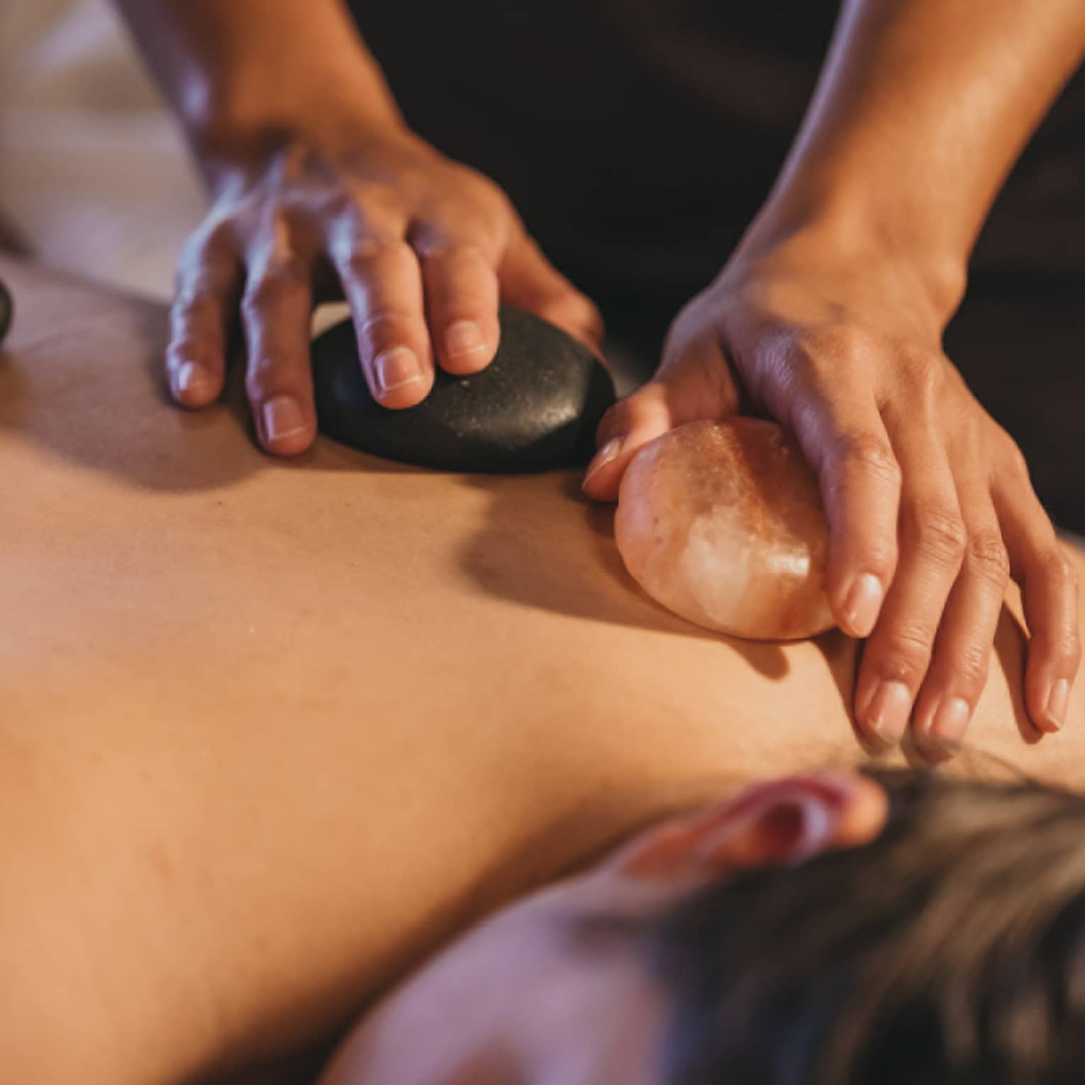 Close up of hands massaging warm stones on a woman's bare back