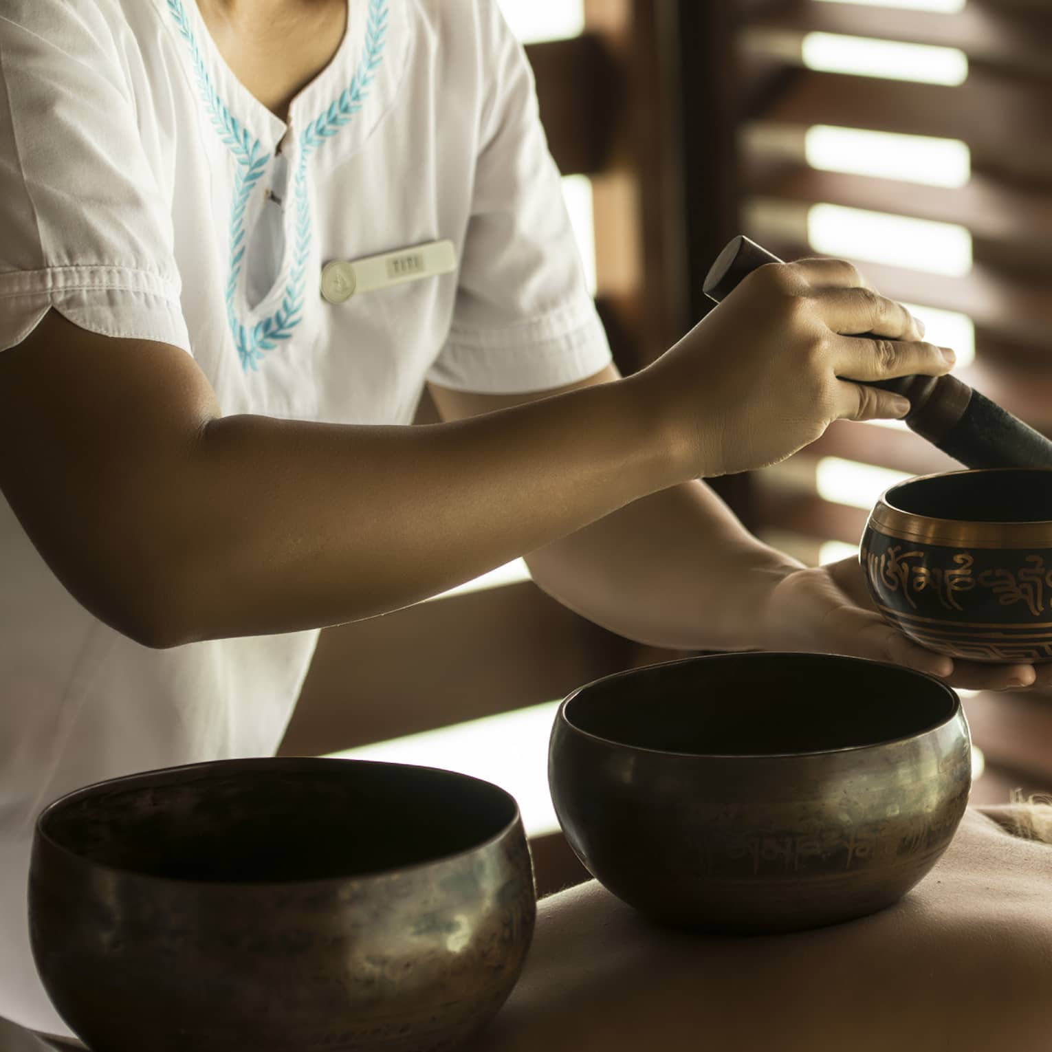 Therapist performing a sound healing ritual with singing bowls on a relaxed spa guest