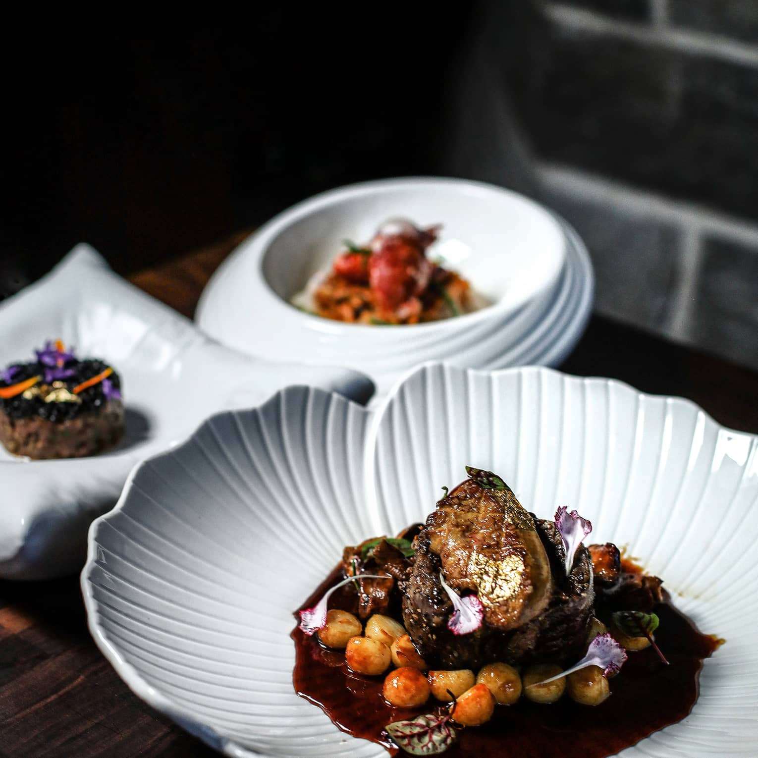 Three white plates of food set on a dark table with a dark backdrop