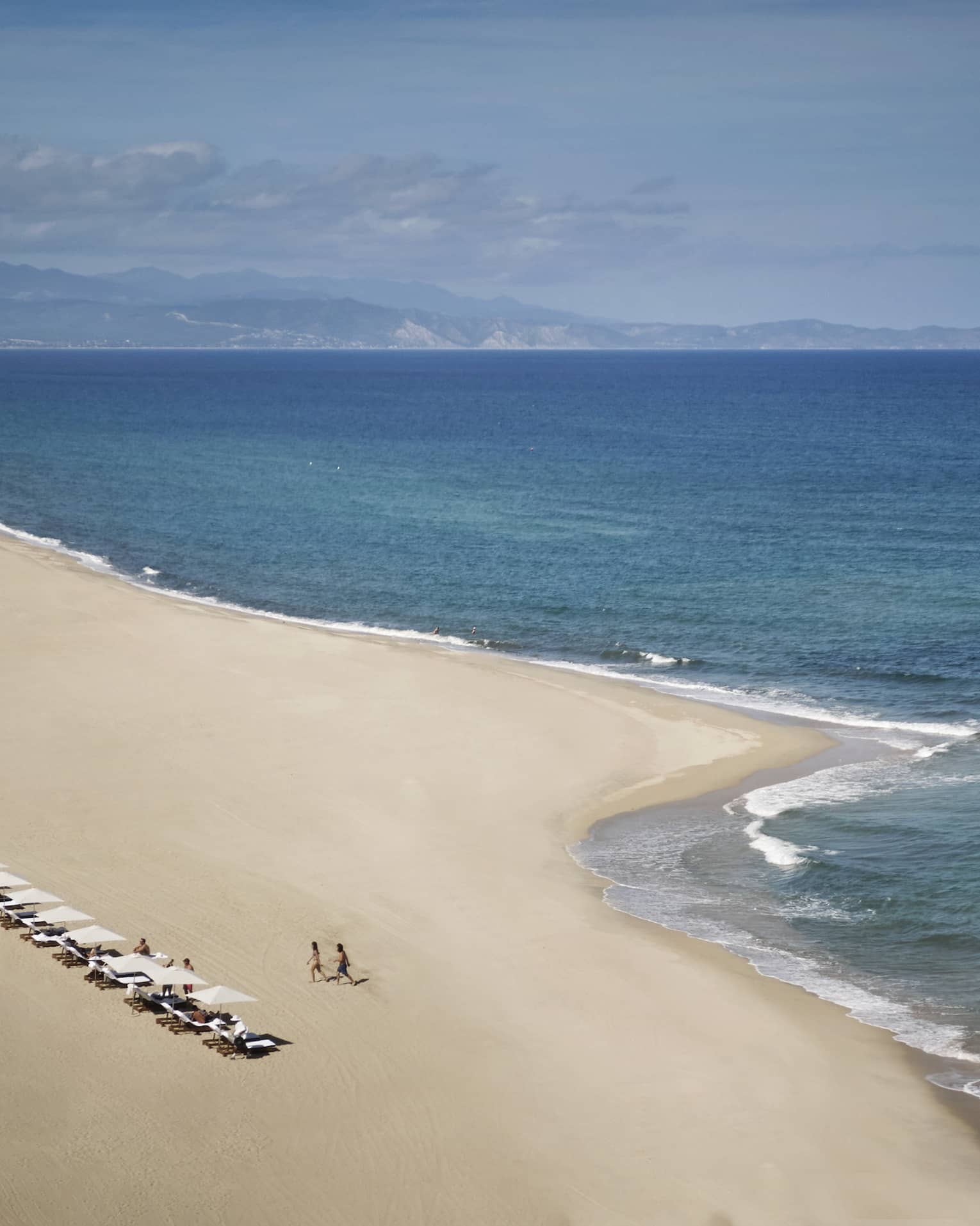 a large white-sand beach with a row of white umbrellas and lounge chairs