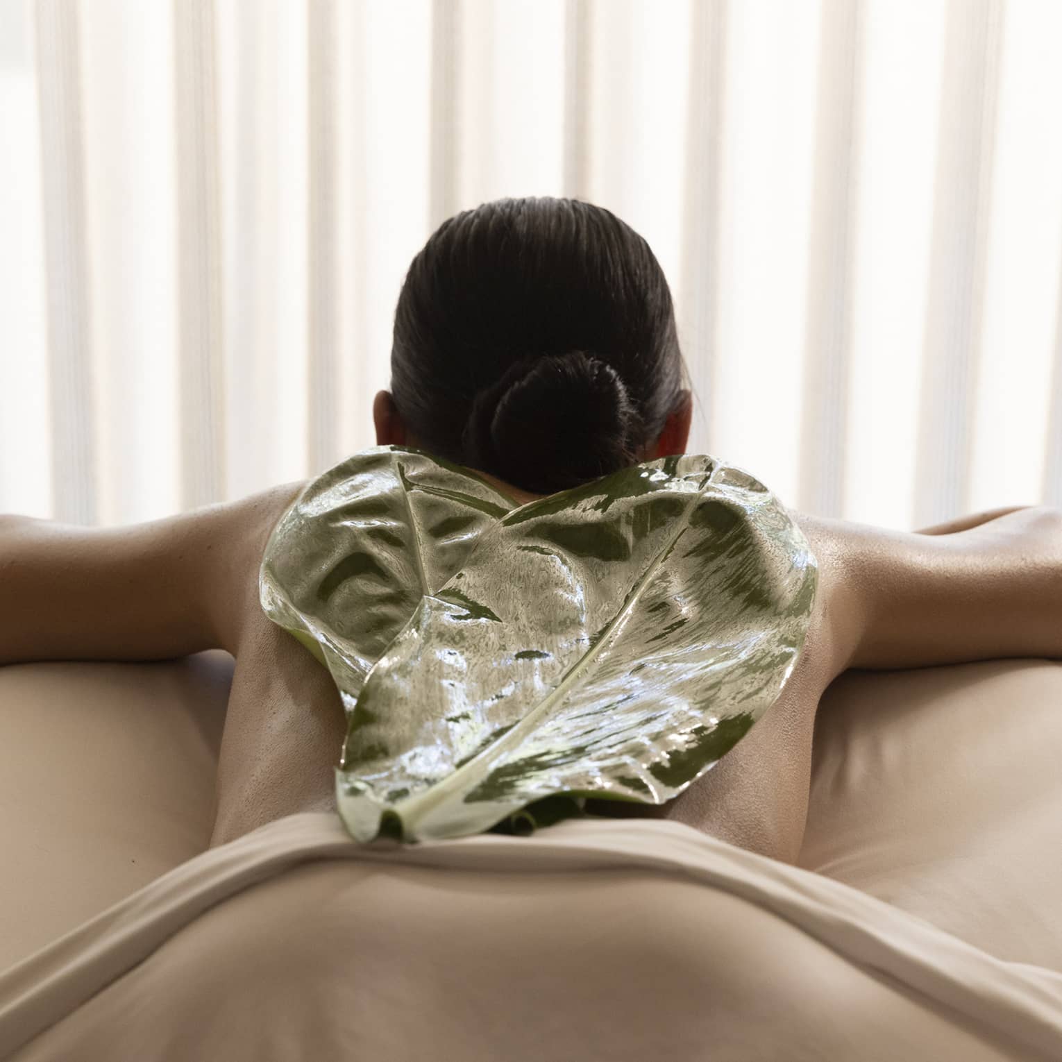 Woman on spa treatment table with Hawaiian tea leaf on back