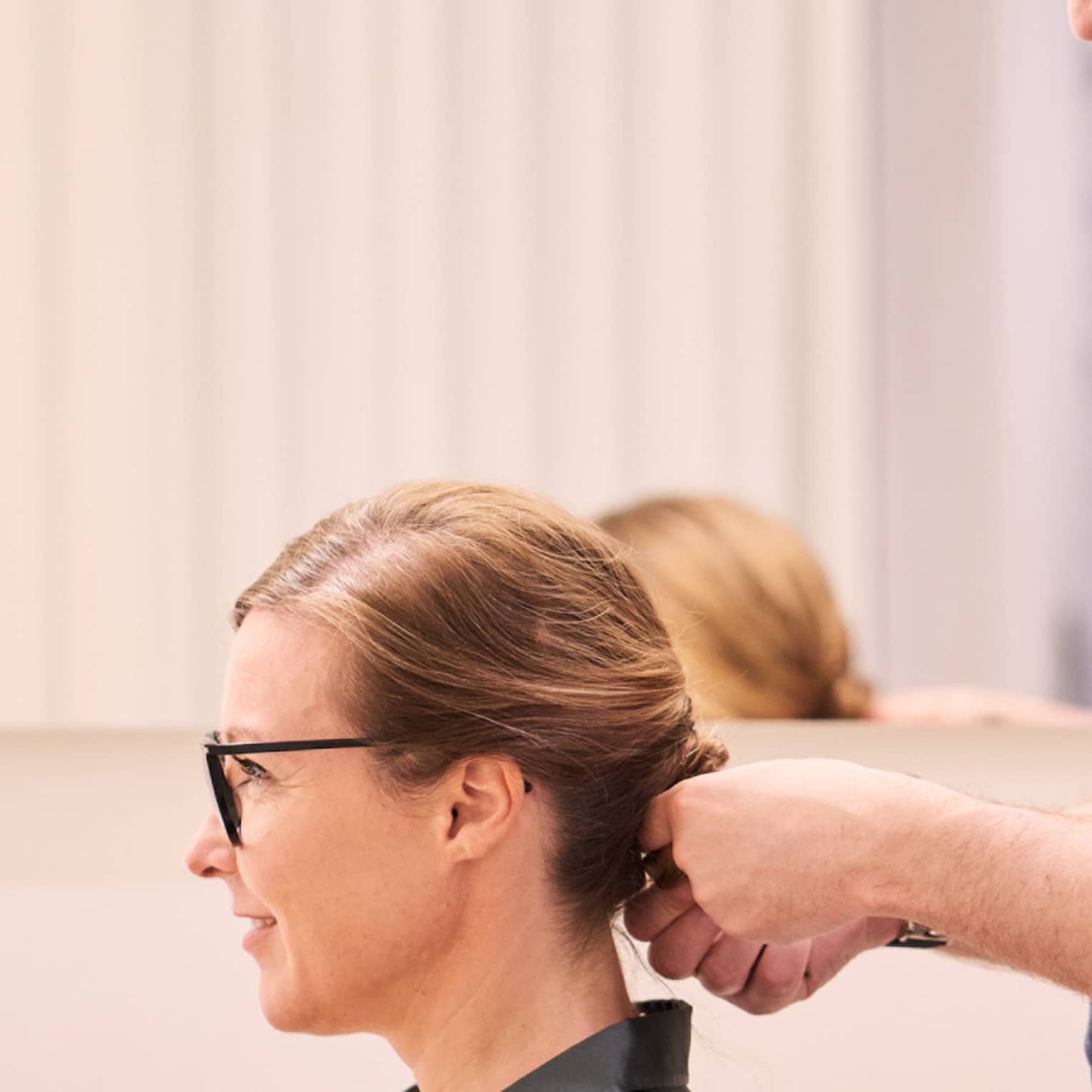 Woman sits in salon chair as hair stylist with long beard holds her hair