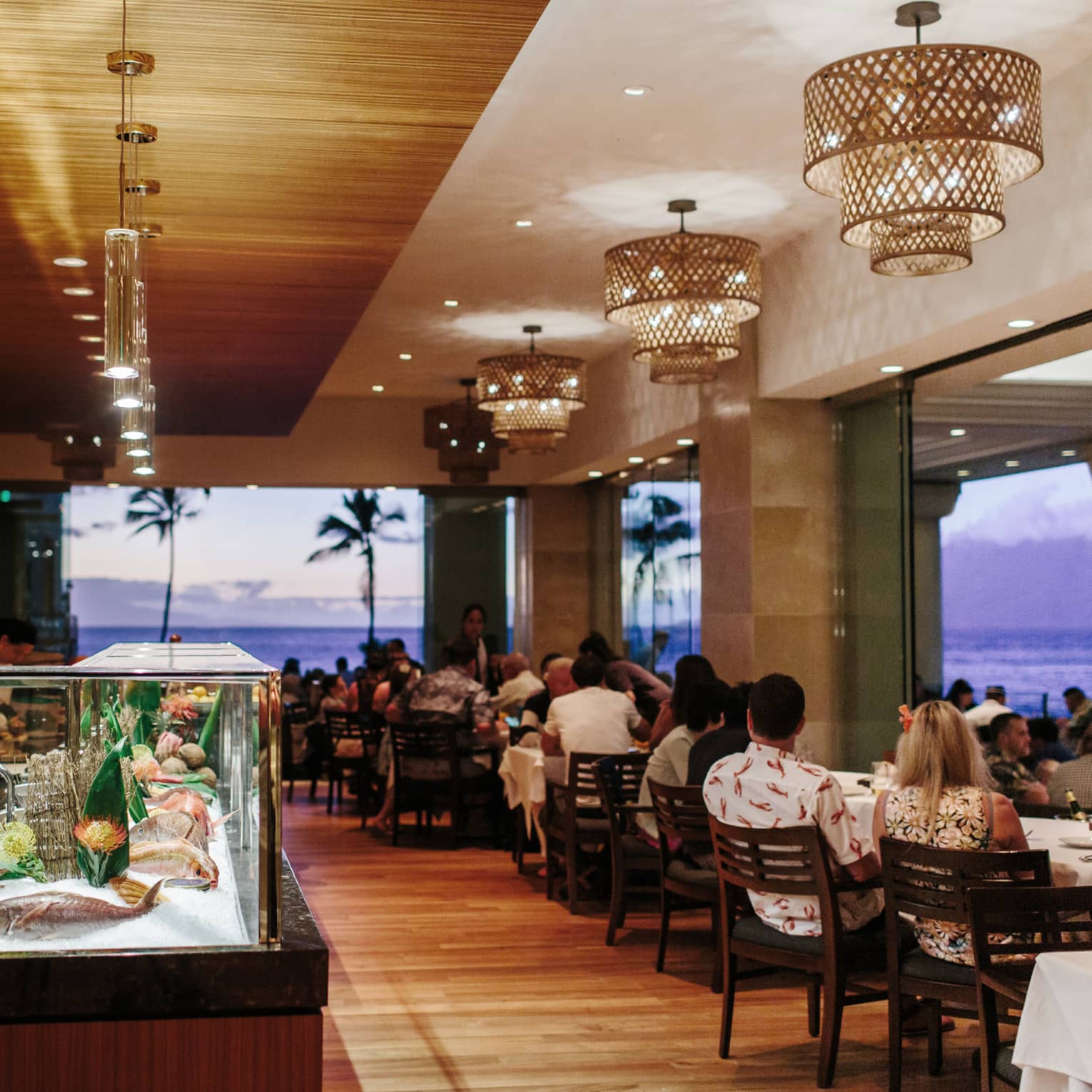 Chef prepares seafood at a sushi bar in a beachfront restaurant during sunset
