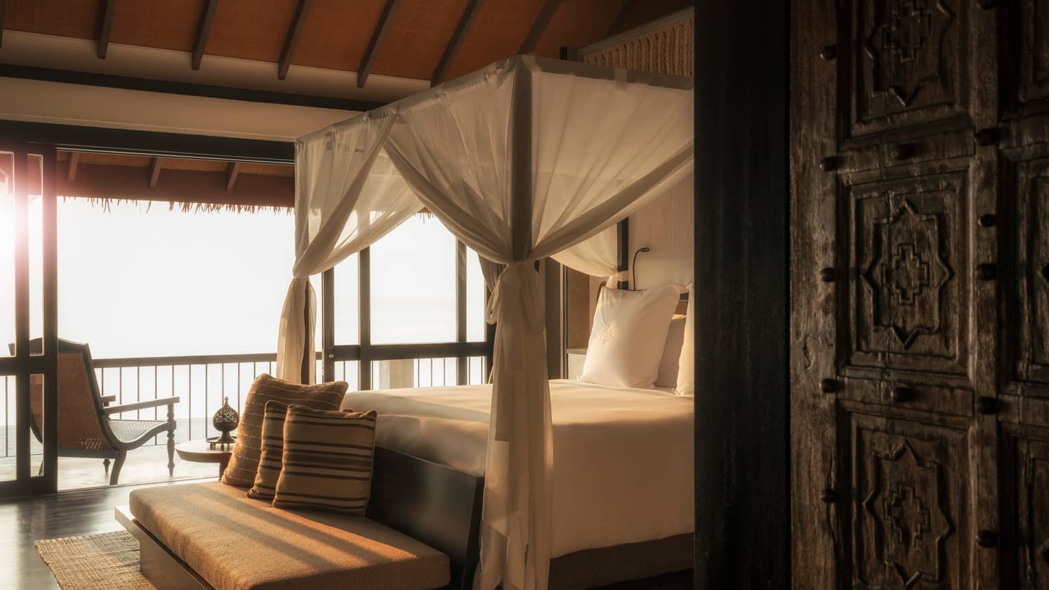 Mezzanine Suites cushioned bench with pillow at foot of canopy bed with white curtains in sunlight