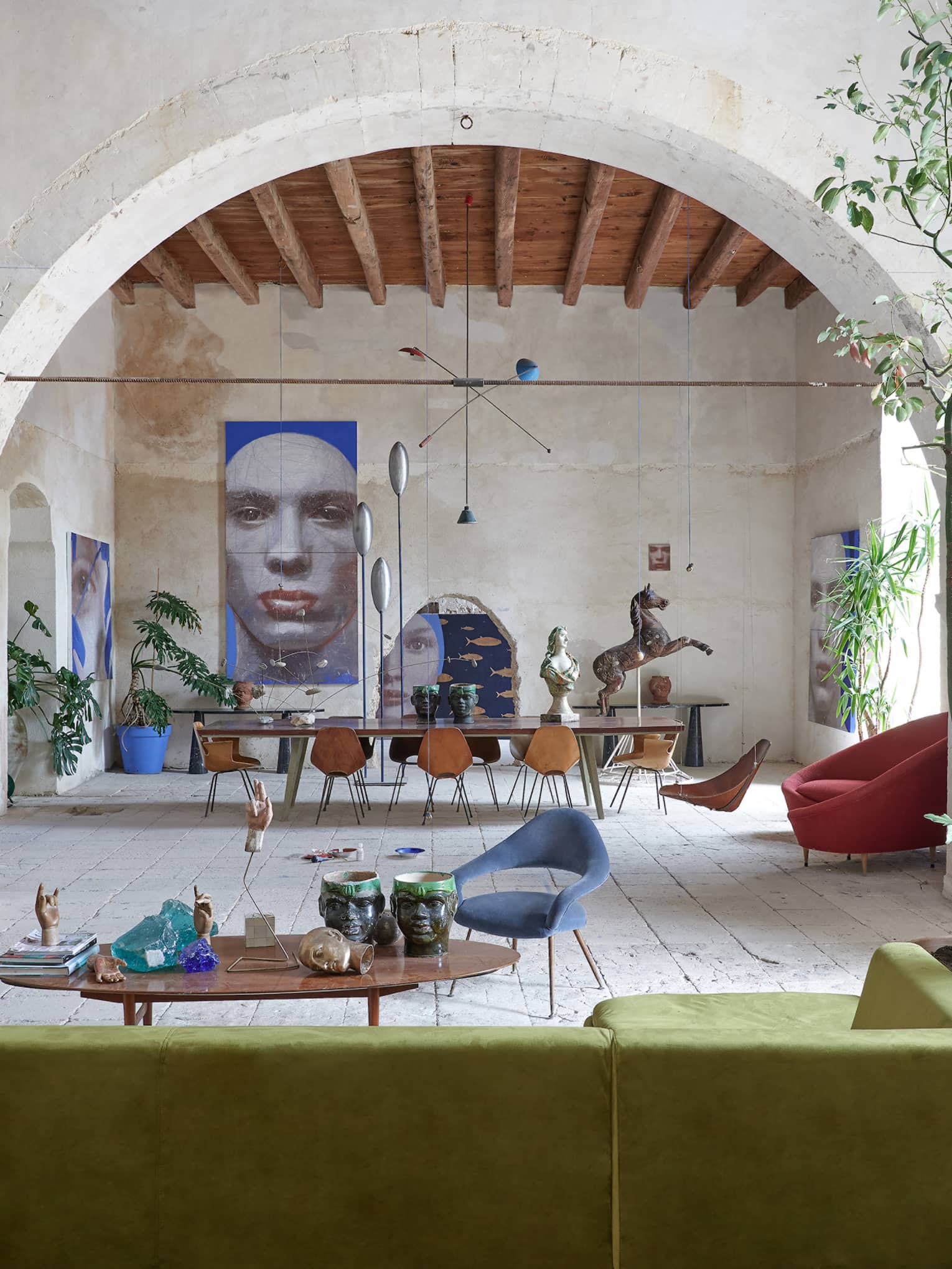 Large room with tropical plants, contemporary furnishings, an arched stone wall and artwork in the distance