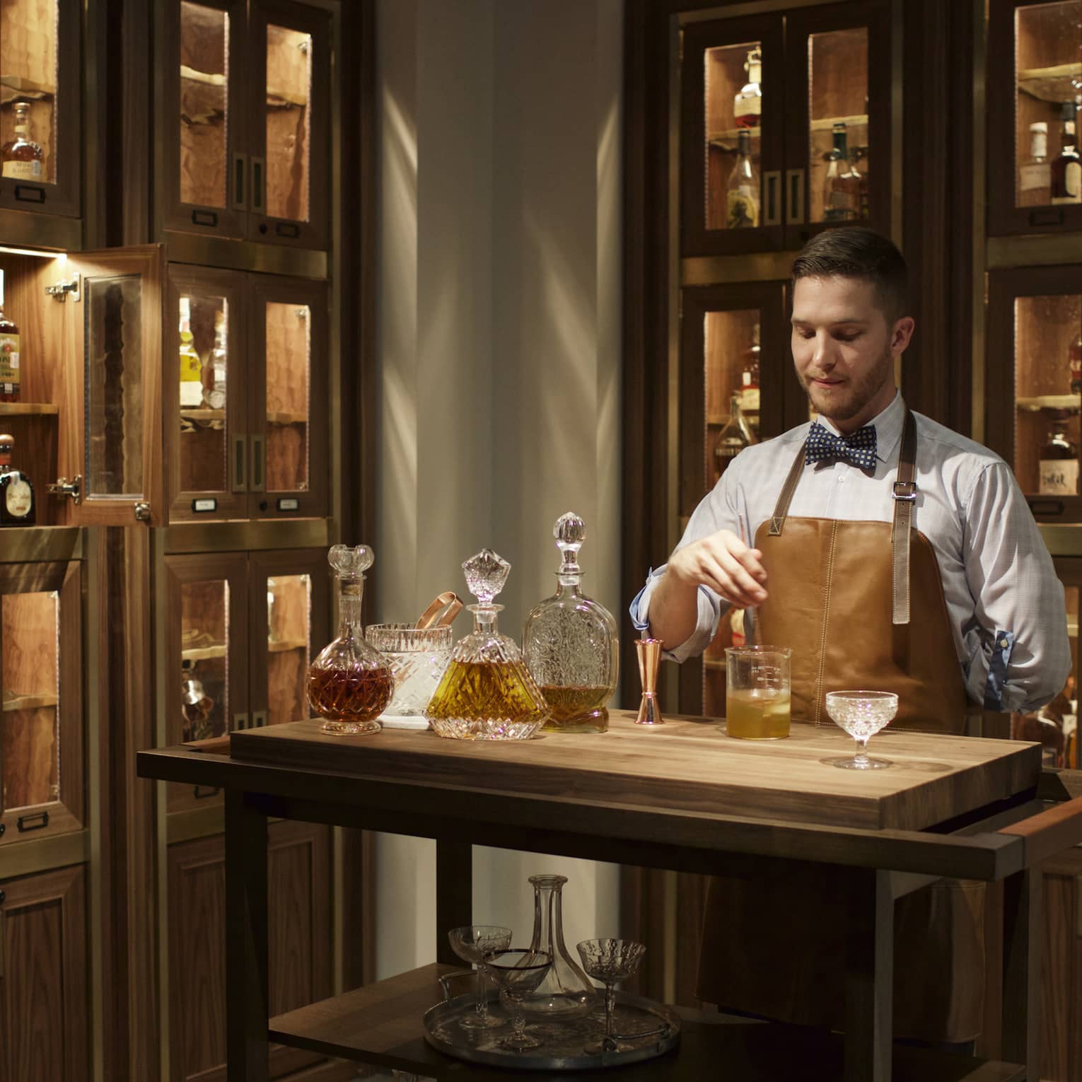 Bayou & Bottle mixologist in apron stirs bourbon cocktail, surrounded by illuminated display cases with bottles