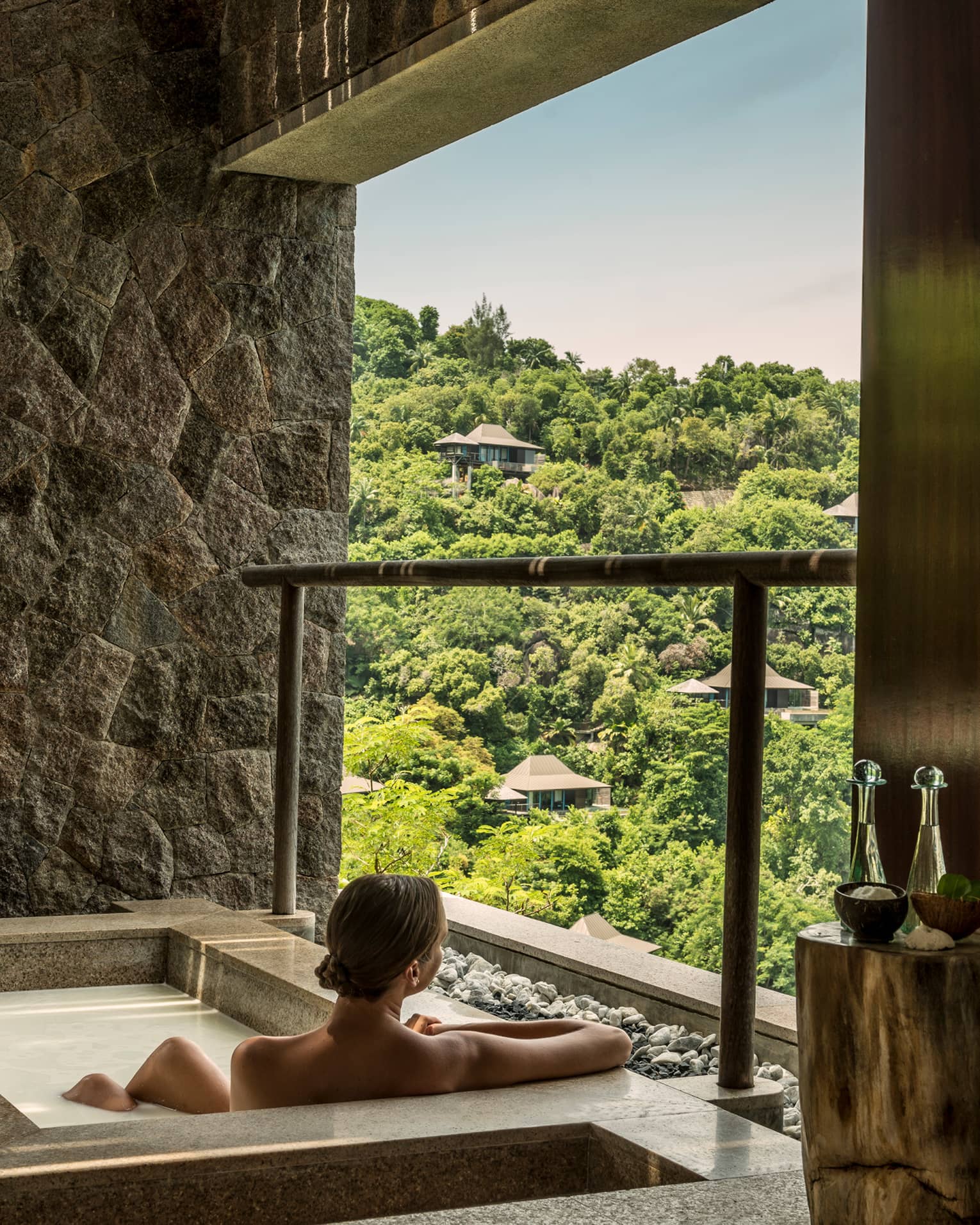 Back of woman sitting in rectangular hot tub, looking out open wall at mountain