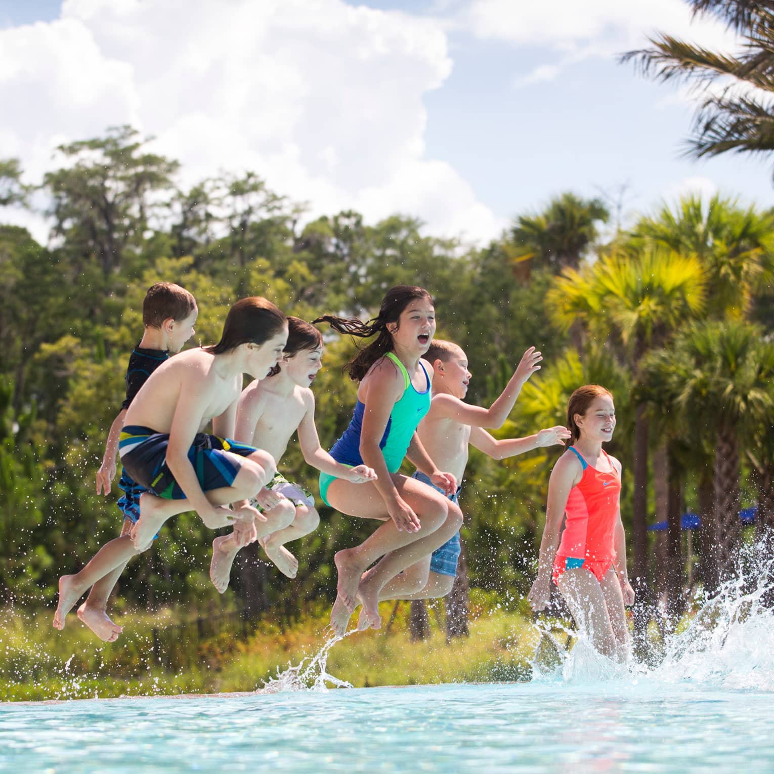 Group of children wearing swimsuits jump into outdoor swimming pool