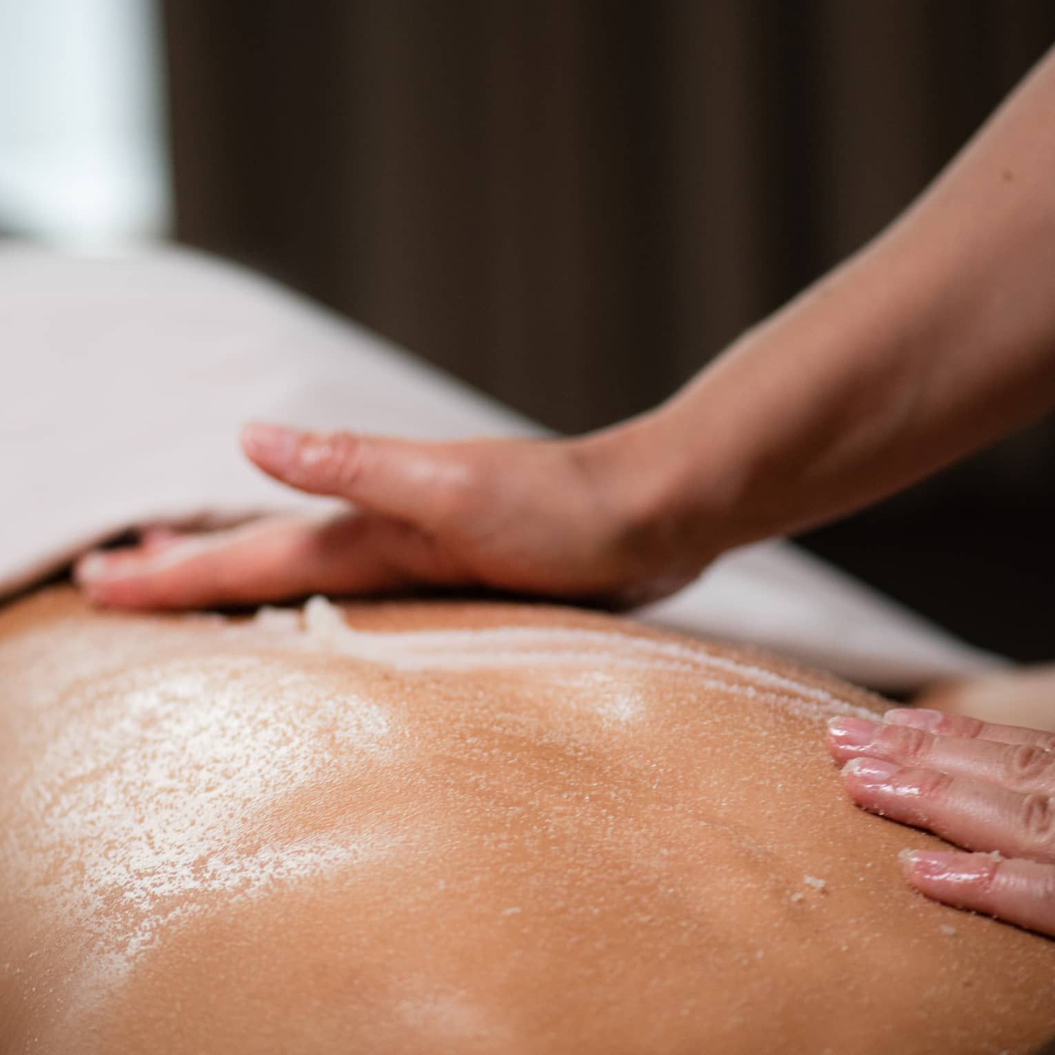 A masseuse spreads a cream across a woman's back as she lies on a massage table.