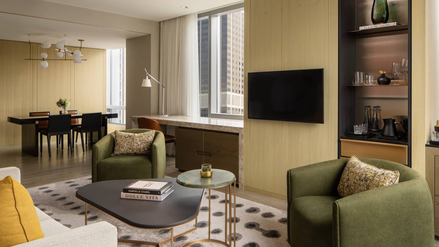 Luxury suite living area with a dining table and four chairs, desk, green armchairs, beige sofa, bar cabinet with glassware, TV and large windows