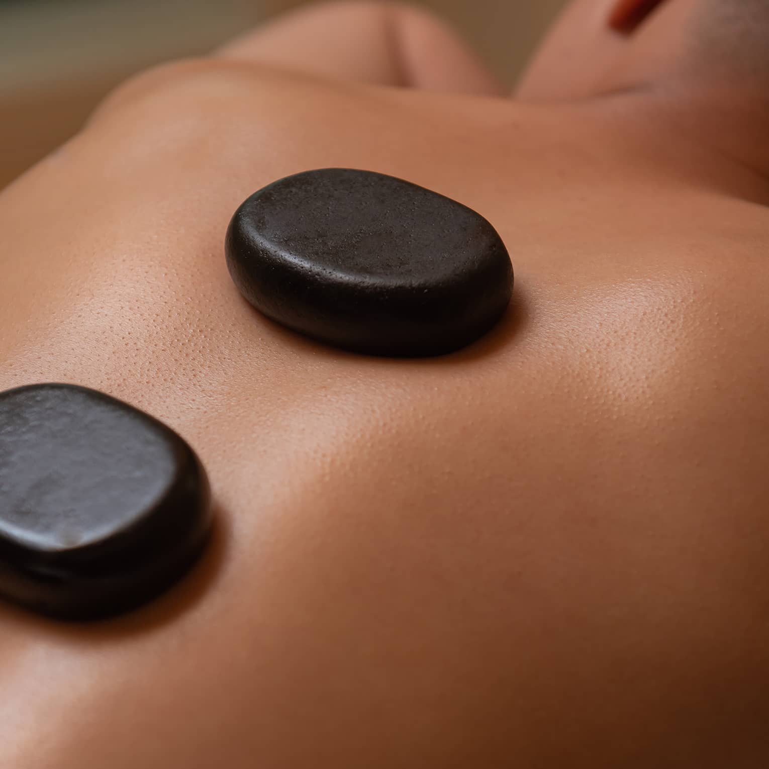 Three large black stones rest on man's bare back and spine as he lays on massage table