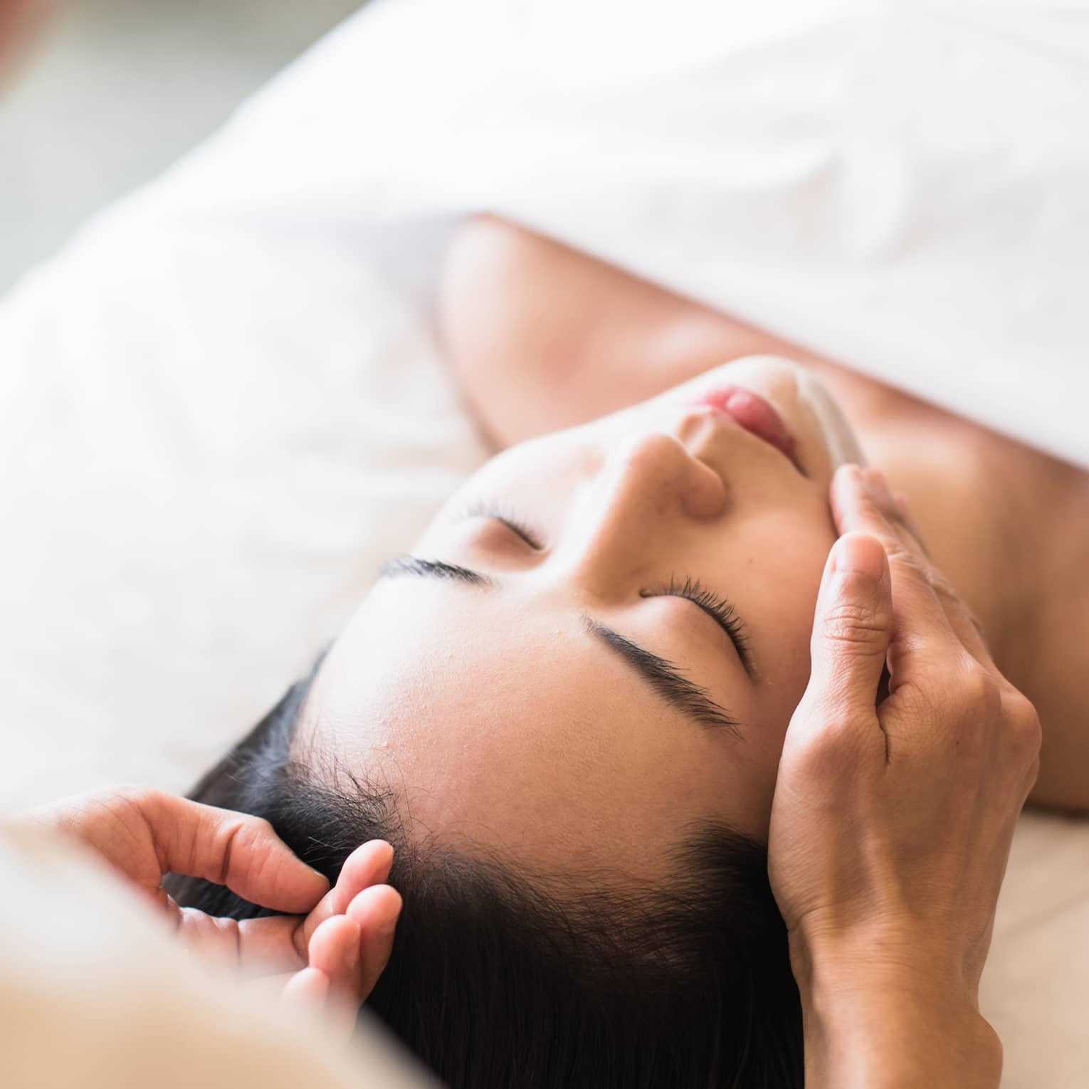 A guest receiving a soothing facial at a spa, lying on a massage table, surrounded by calming décor and soft lighting.