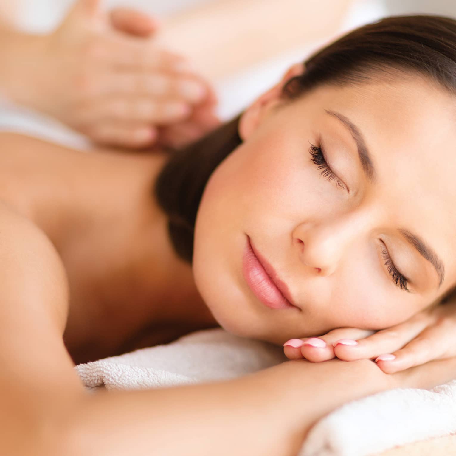 Woman lies on massage table, closes eyes. rests head on arms as spa staff massages back