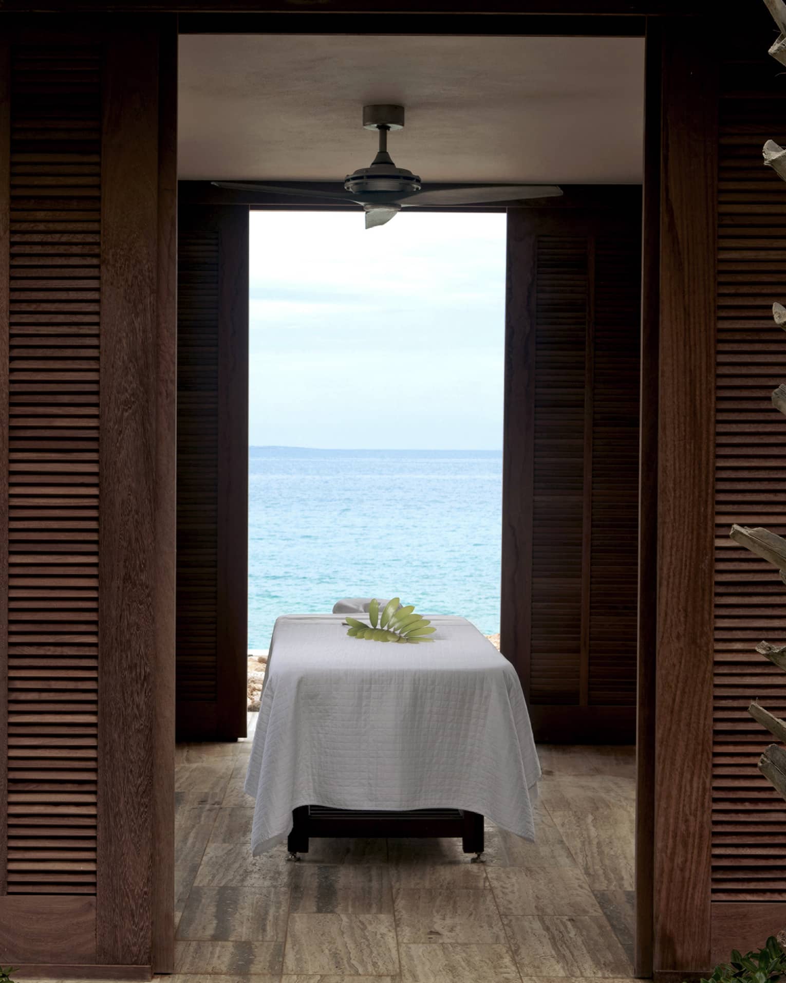 Massage table with white sheet under outdoor pavilion with wood shutters