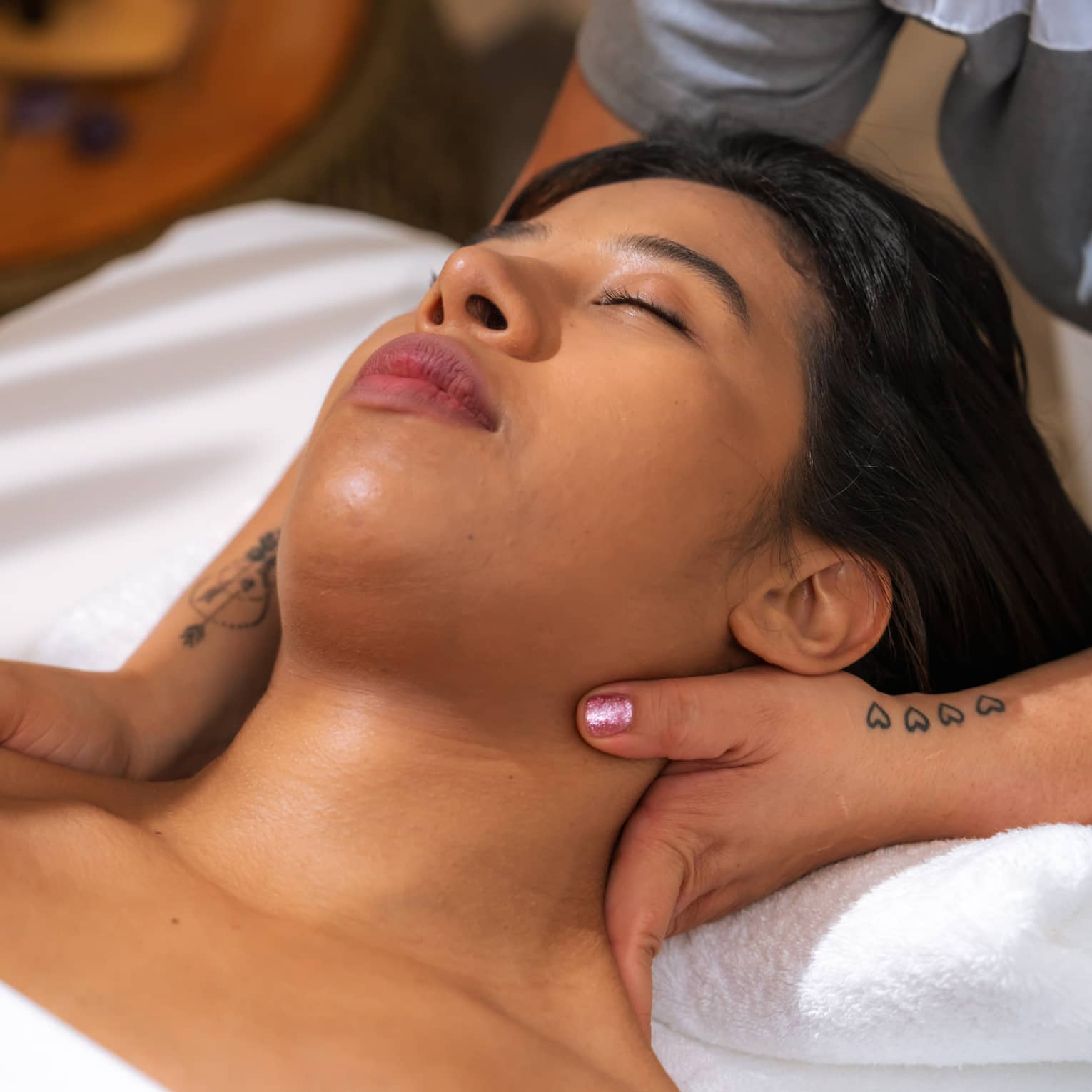Woman relaxes with eyes closed as massage therapist massages her neck
