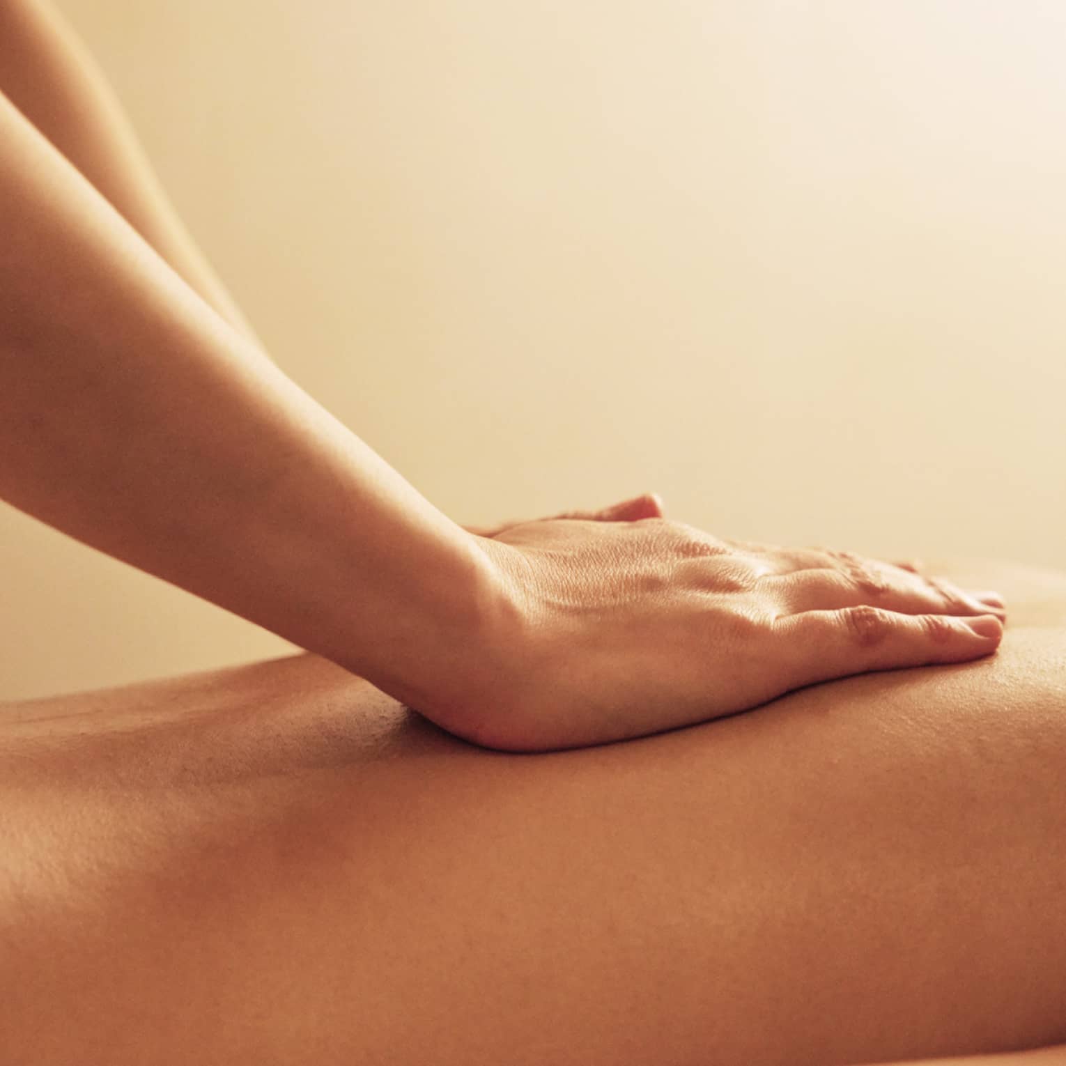 Masseuse rests hands on woman's bare back as she lays on massage table