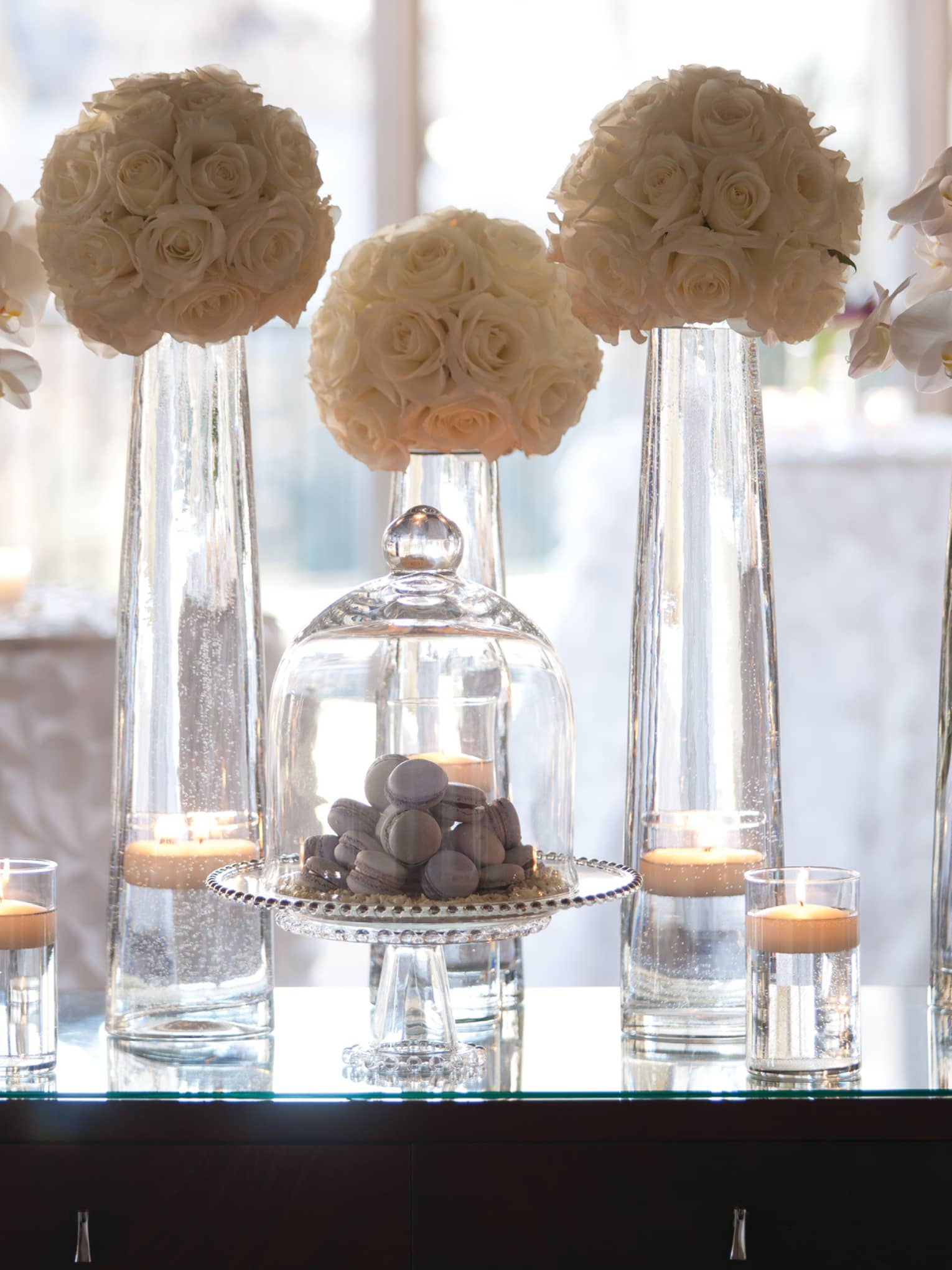 Flowers in tall glass vases, macarons in glass dessert display on table by window